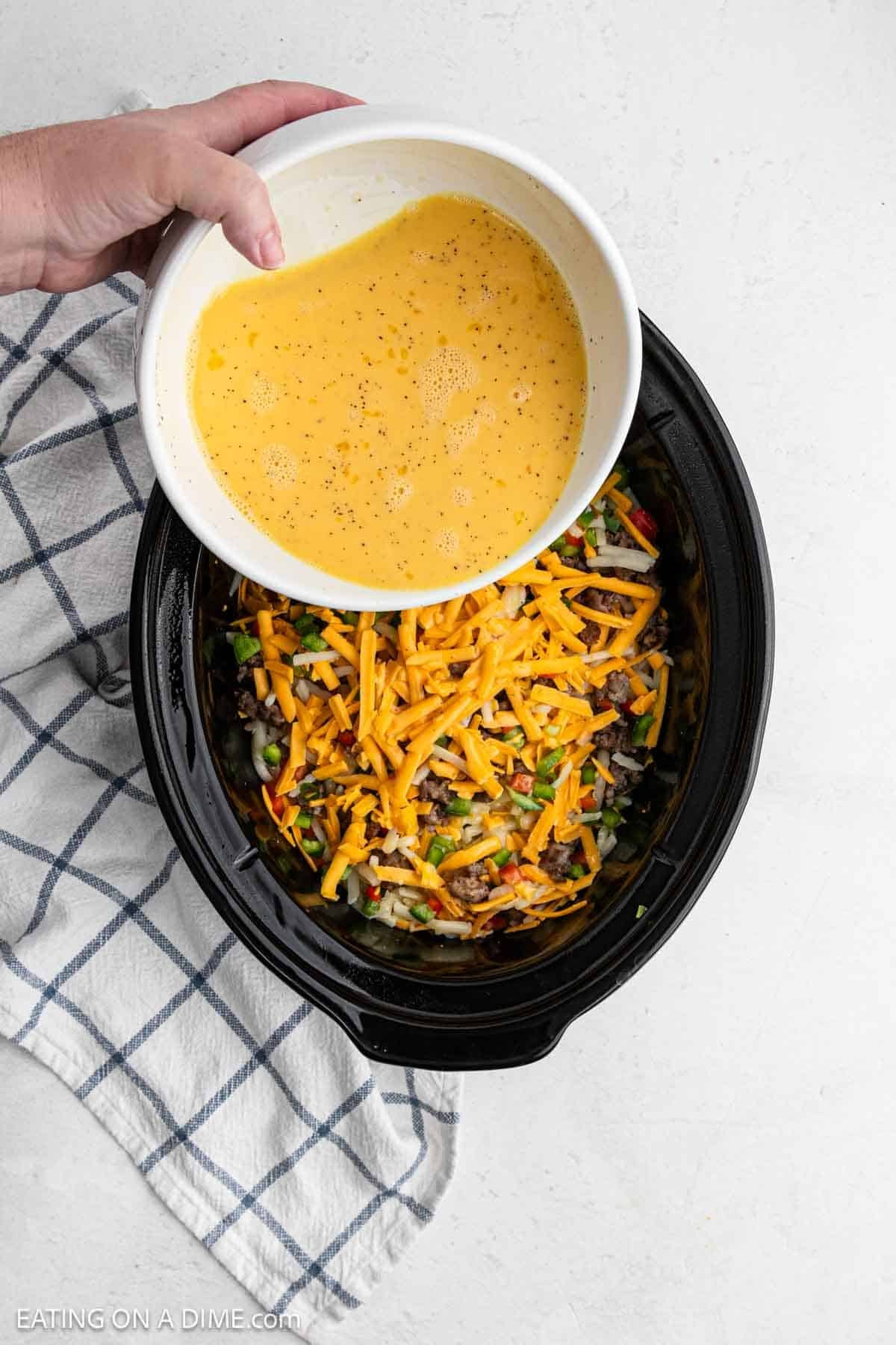 Pouring the egg mixture in the crockpot with the cheese and veggies in the slow cooker.