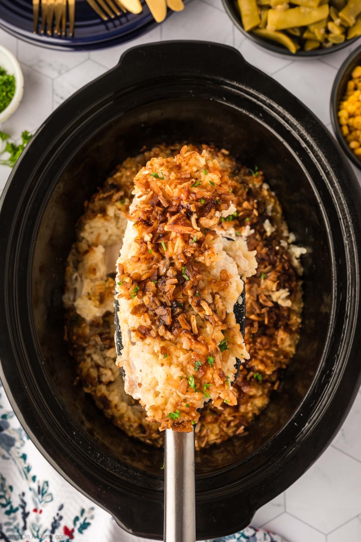 A serving of the no pick chicken on a spatula of a crock pot with the chicken mixture in it. 