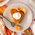 Slice of pumpkin pie on a plate topped with whipped cream