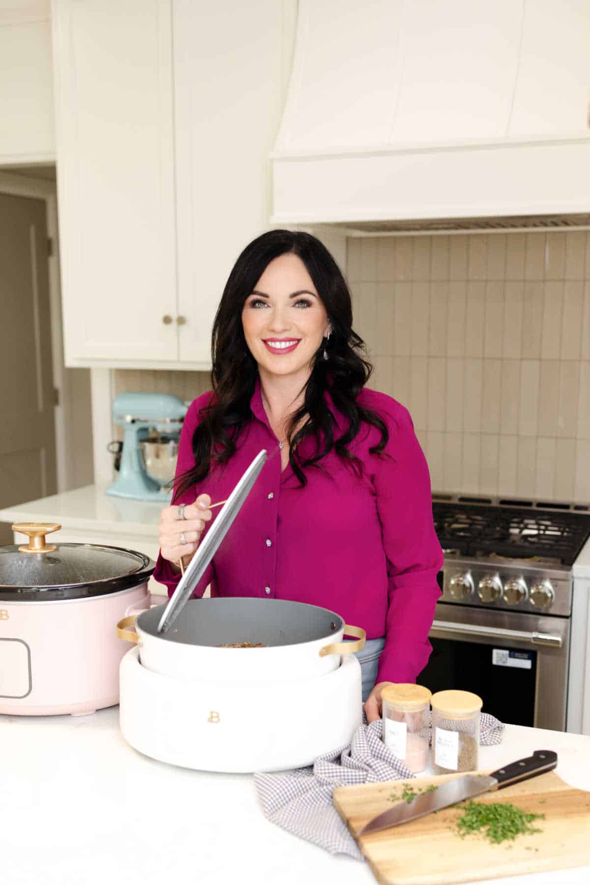 Carrie, the owner with a pink shirt holding the lid of a crock pot while it sits on the counter.