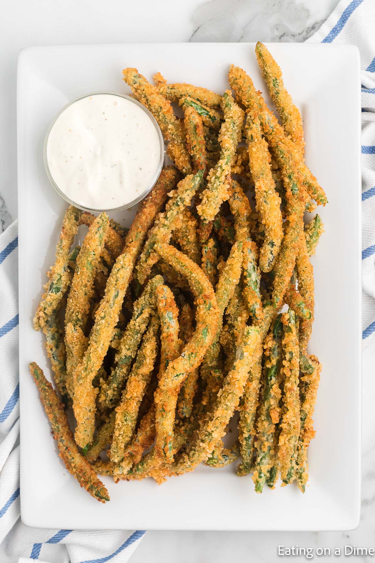 Fried Green Beans stacked on a platter with a side of ranch dressing in a bowl