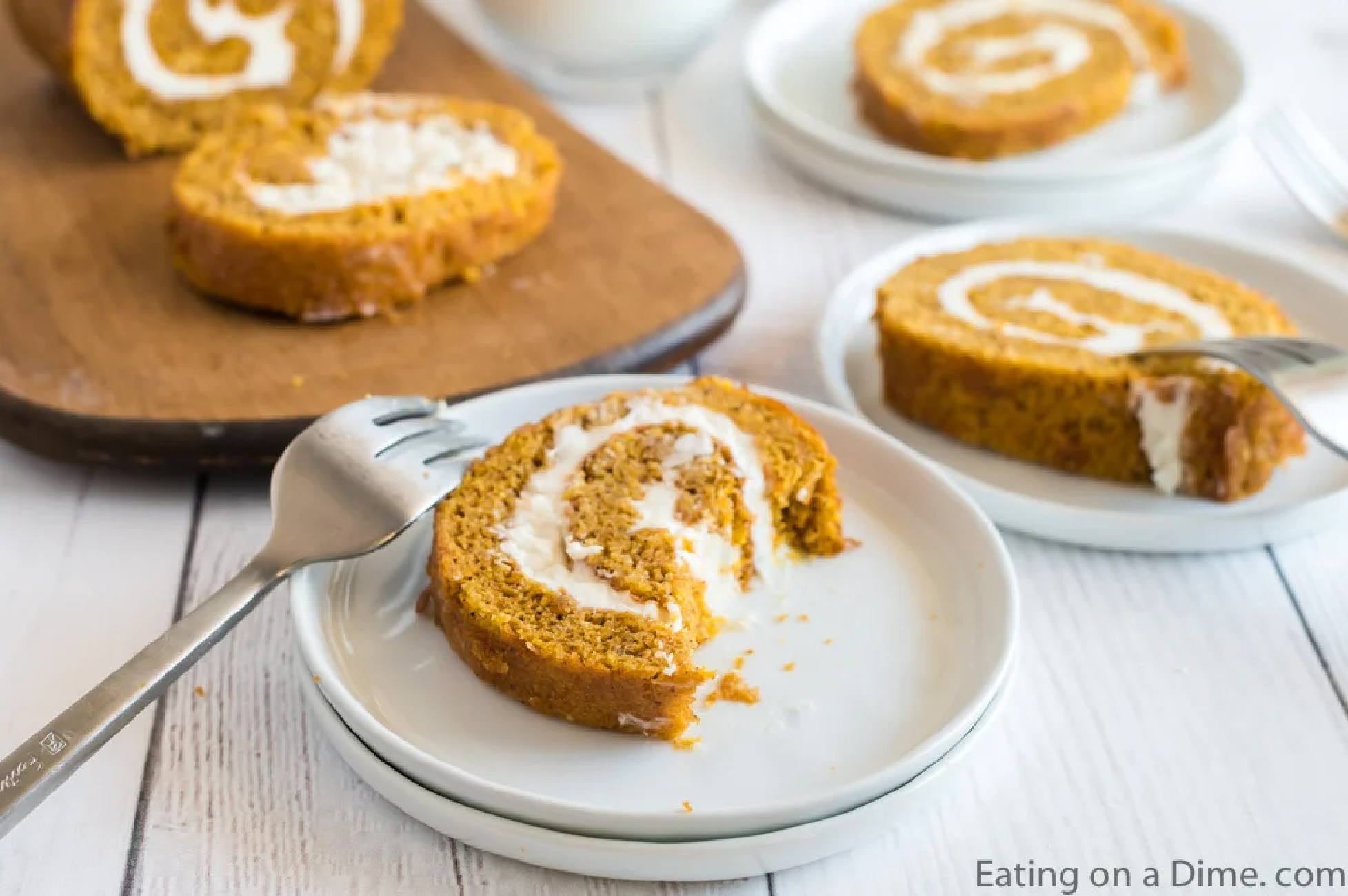Close up image of slices of pumpkin roll on white plates and cutting board with forks. 
