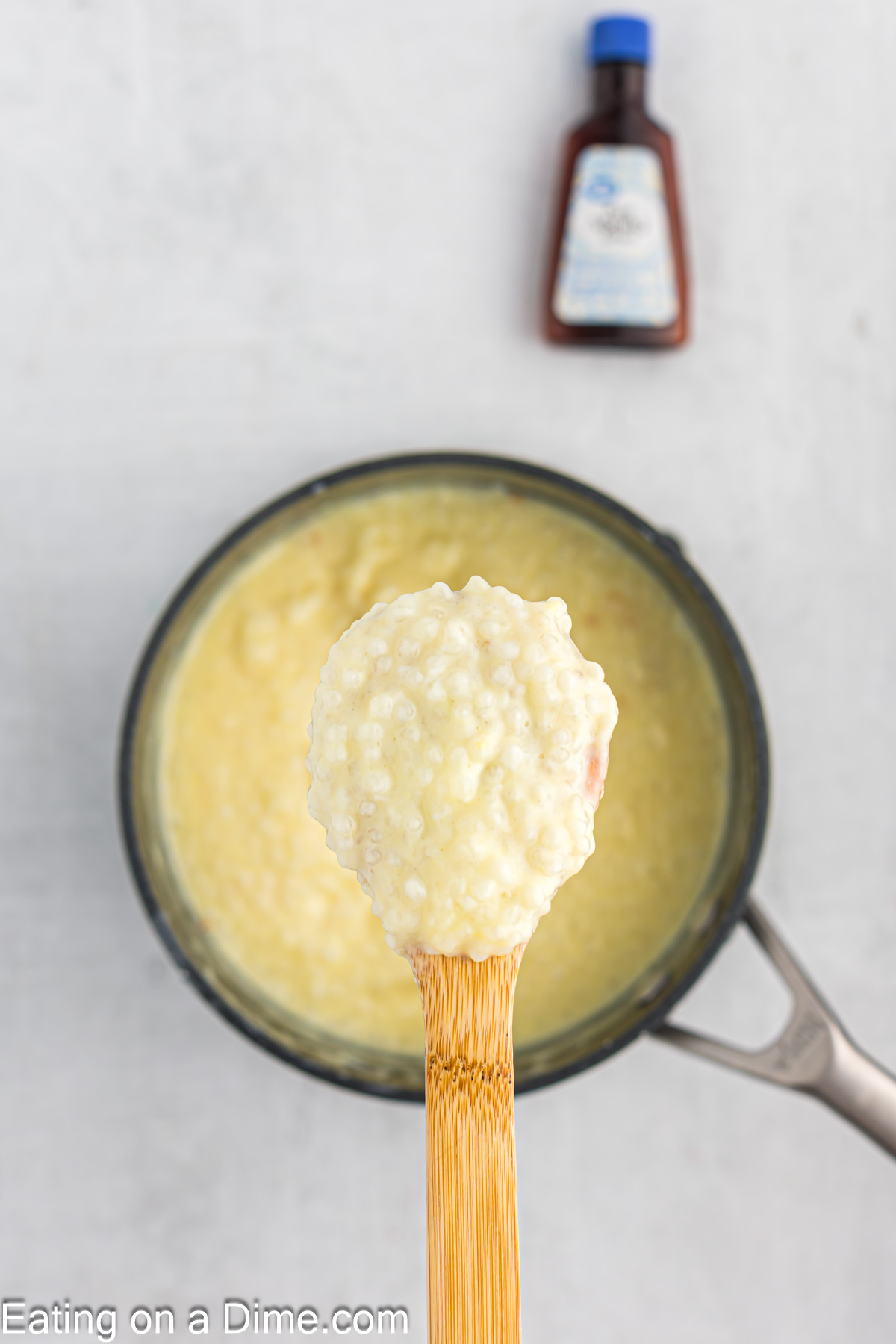 A wooden spoon with a serving of tapioca pudding with a saucepan of pudding in the background