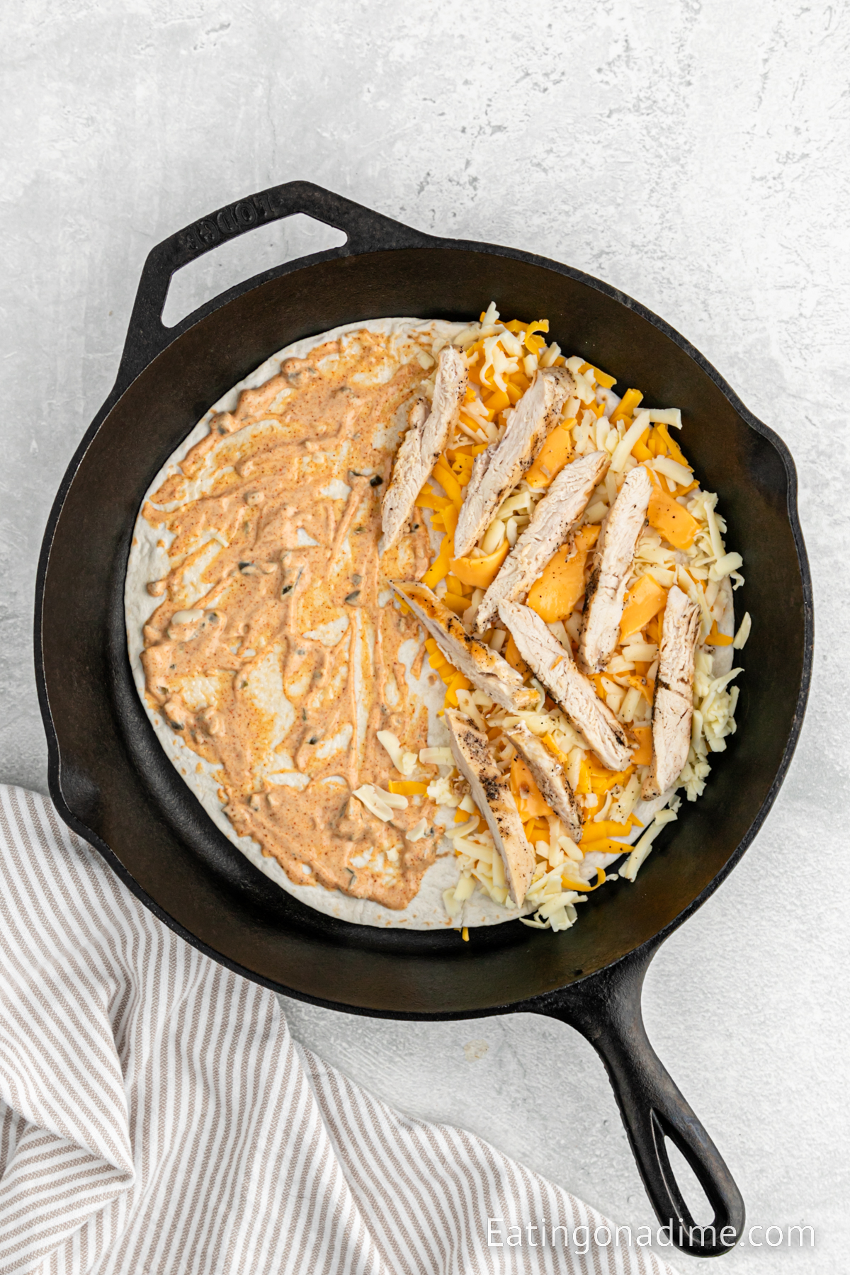 Topping a flour tortilla that is in the skillet with sauce, cheese and chicken