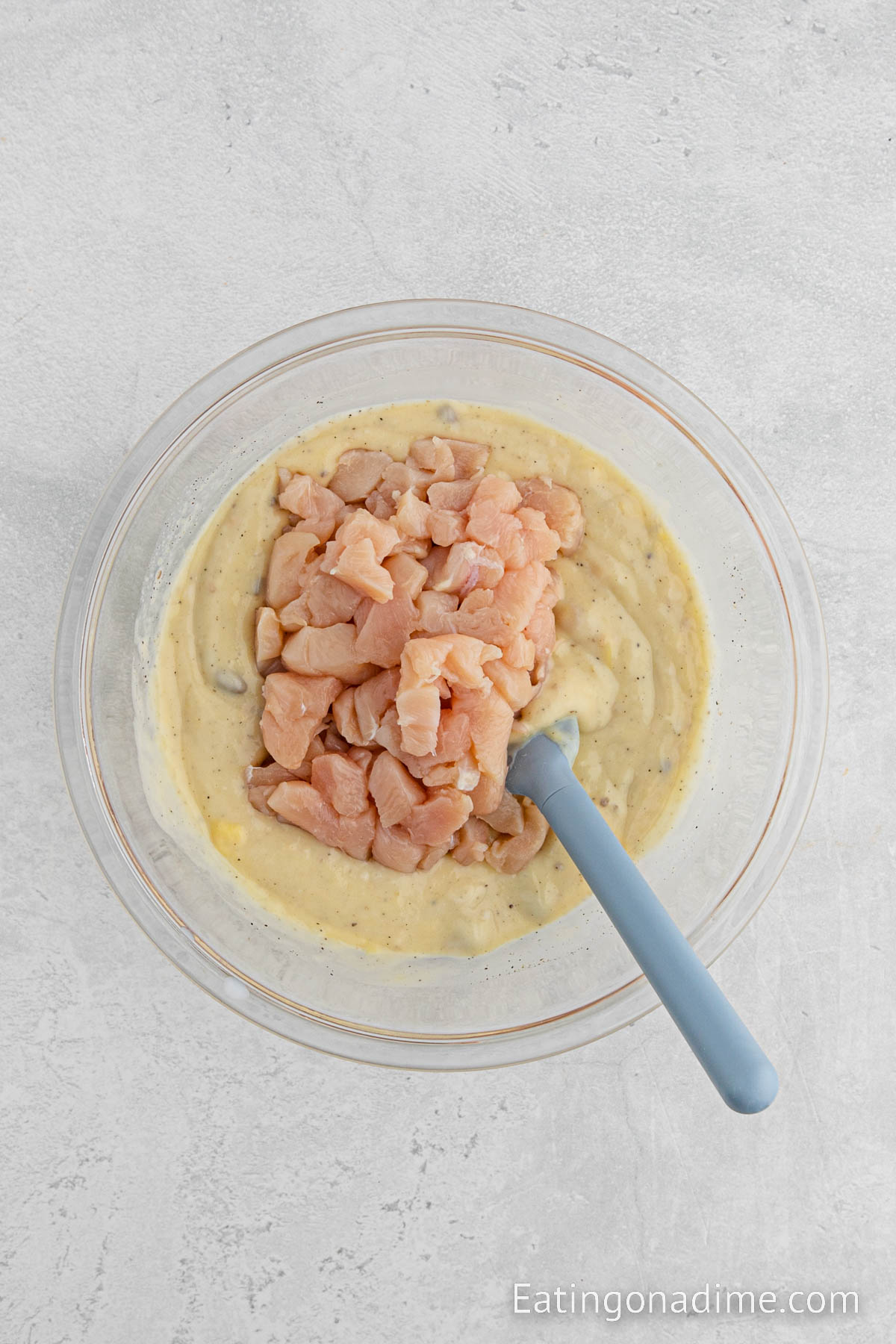 Mixing in diced uncooked chicken in the cream of soup mixture in a bowl