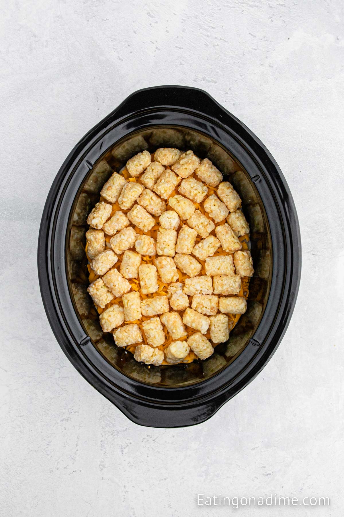 Layering tater tots in the slow cooker on a layer of cheese