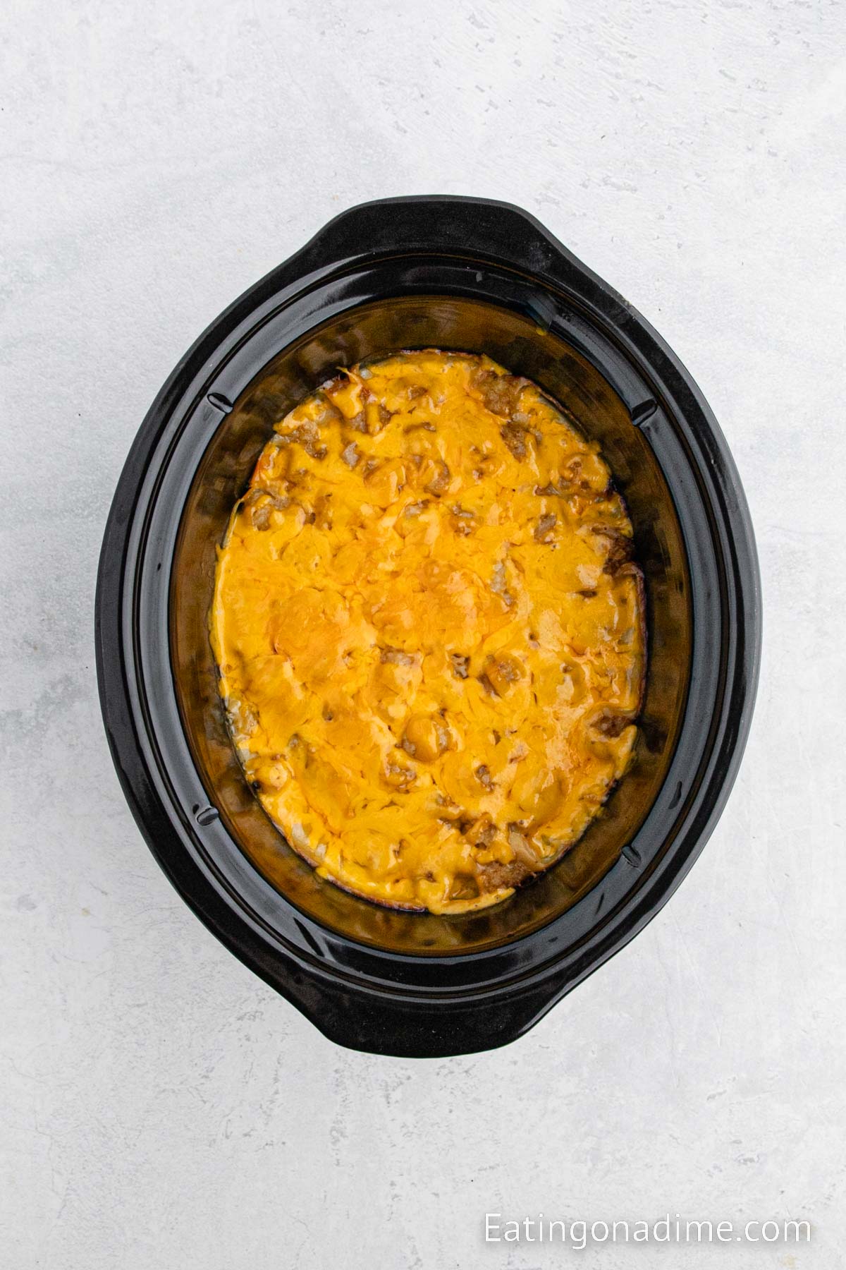 Topping the tater tot casserole with cheese in the slow cooker