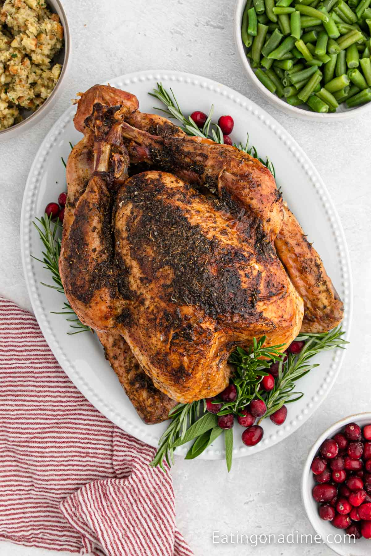 Whole Cooked Turkey on a white platter with fresh herbs and berries and a bowl of green beans and stuffing