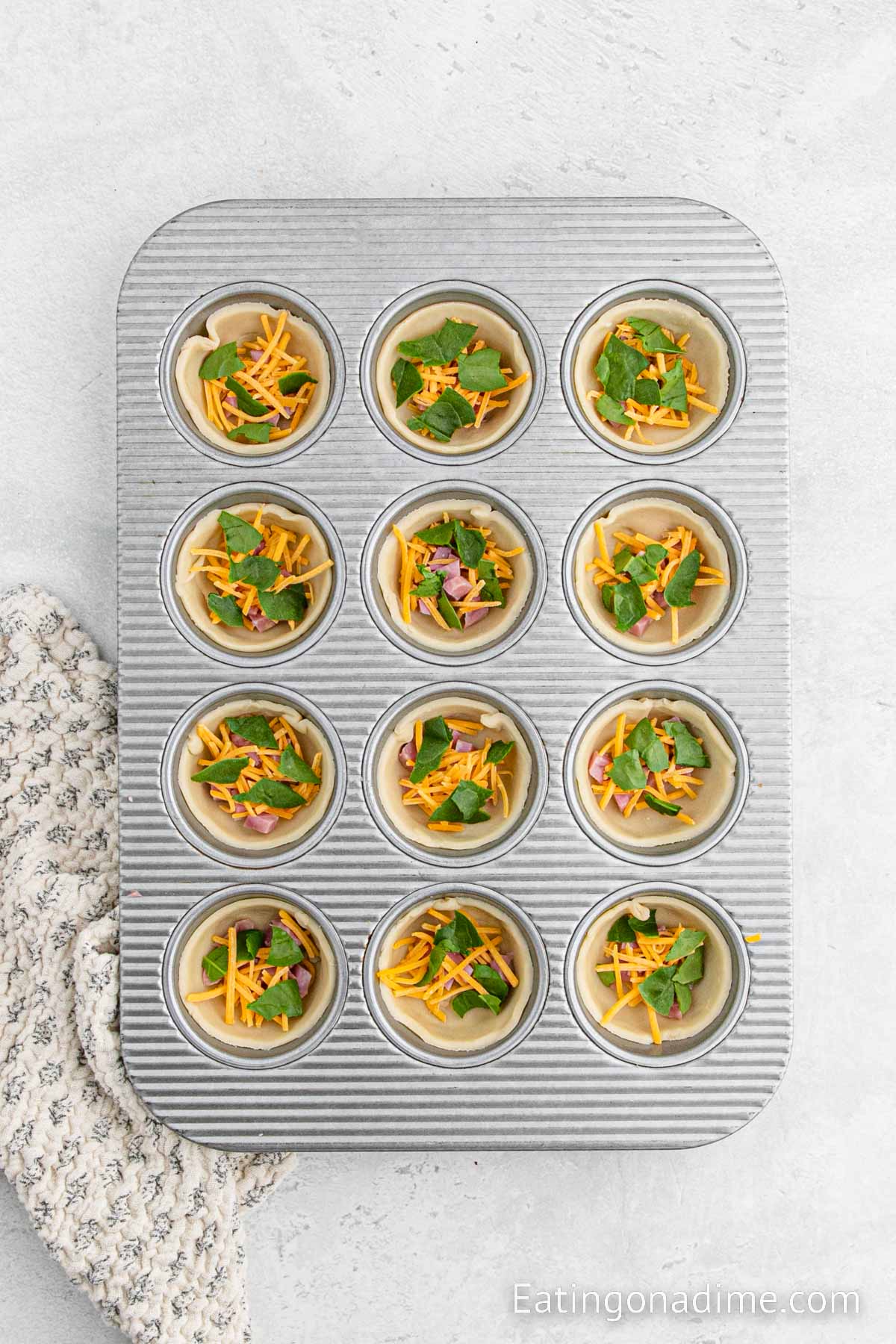 Adding cheese, diced ham and chopped spinach in the muffin tin