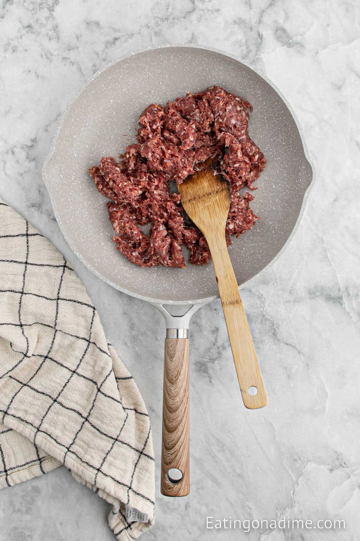 Cooking the ground sausage in a skillet with a wooden spoon
