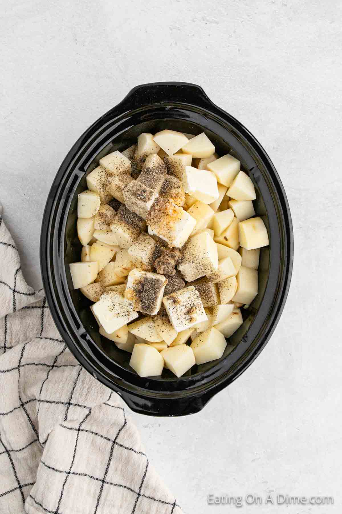 Placing cut potatoes in the slow cooker and topping with butter and seasoning