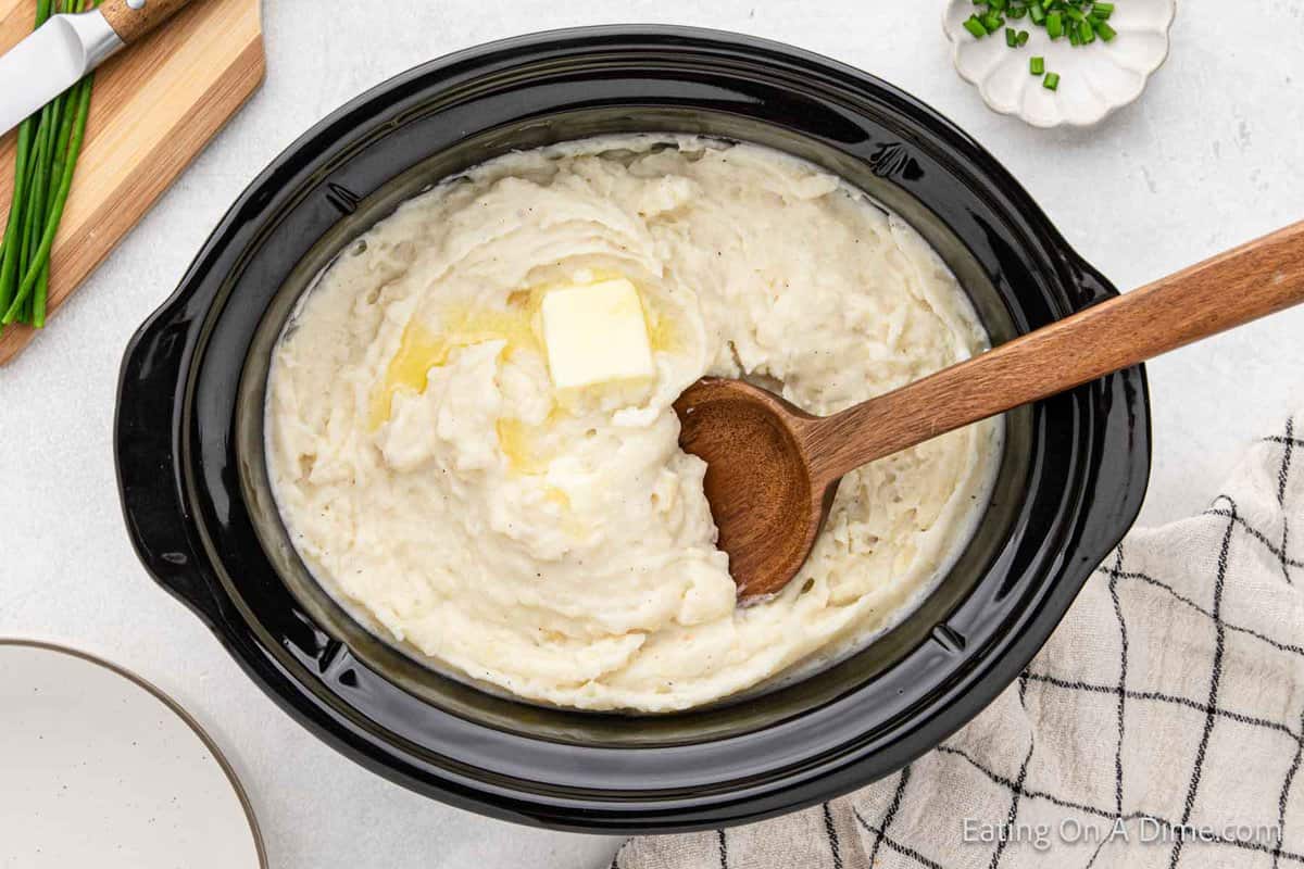 Mashed potatoes in a crock pot topped with butter and a wooden spoon