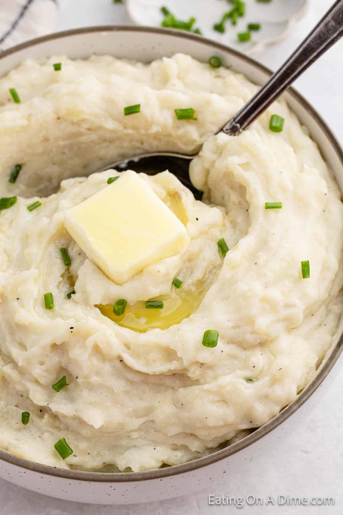 Close up image of mashed potatoes in a bowl topped with butter and chives