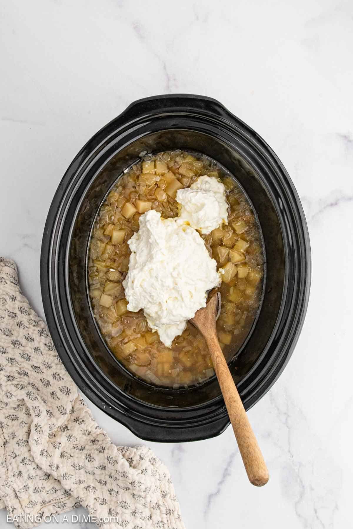 Adding the sour cream mixture in the slow cooker with the cooked potatoes and broth