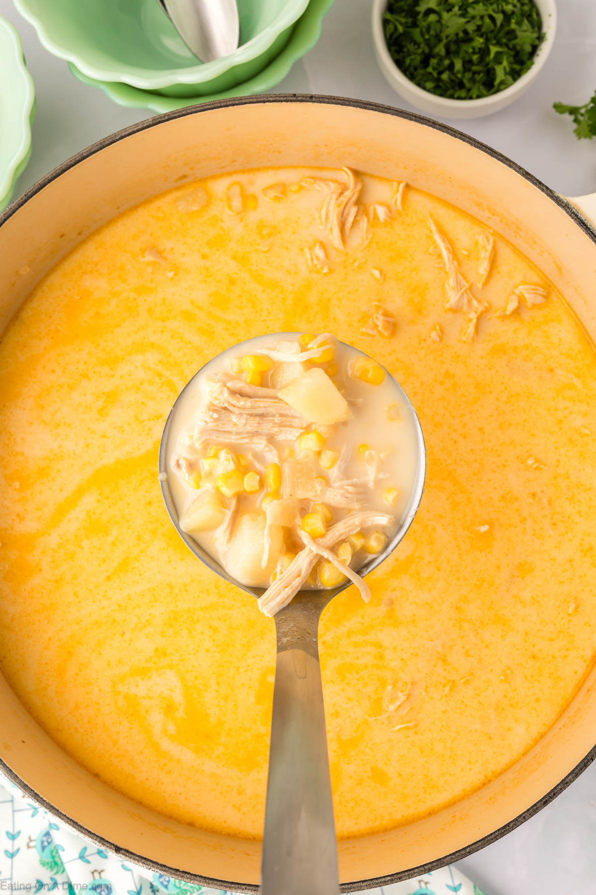 Close up image of chicken corn soup on a ladle over a large pot of soup