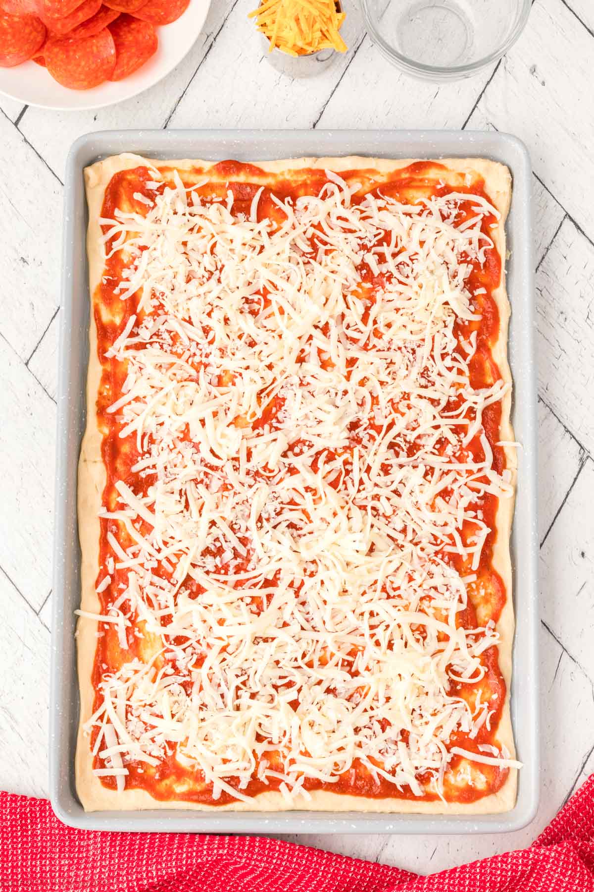 Topping shredded cheese over the pizza sauce
