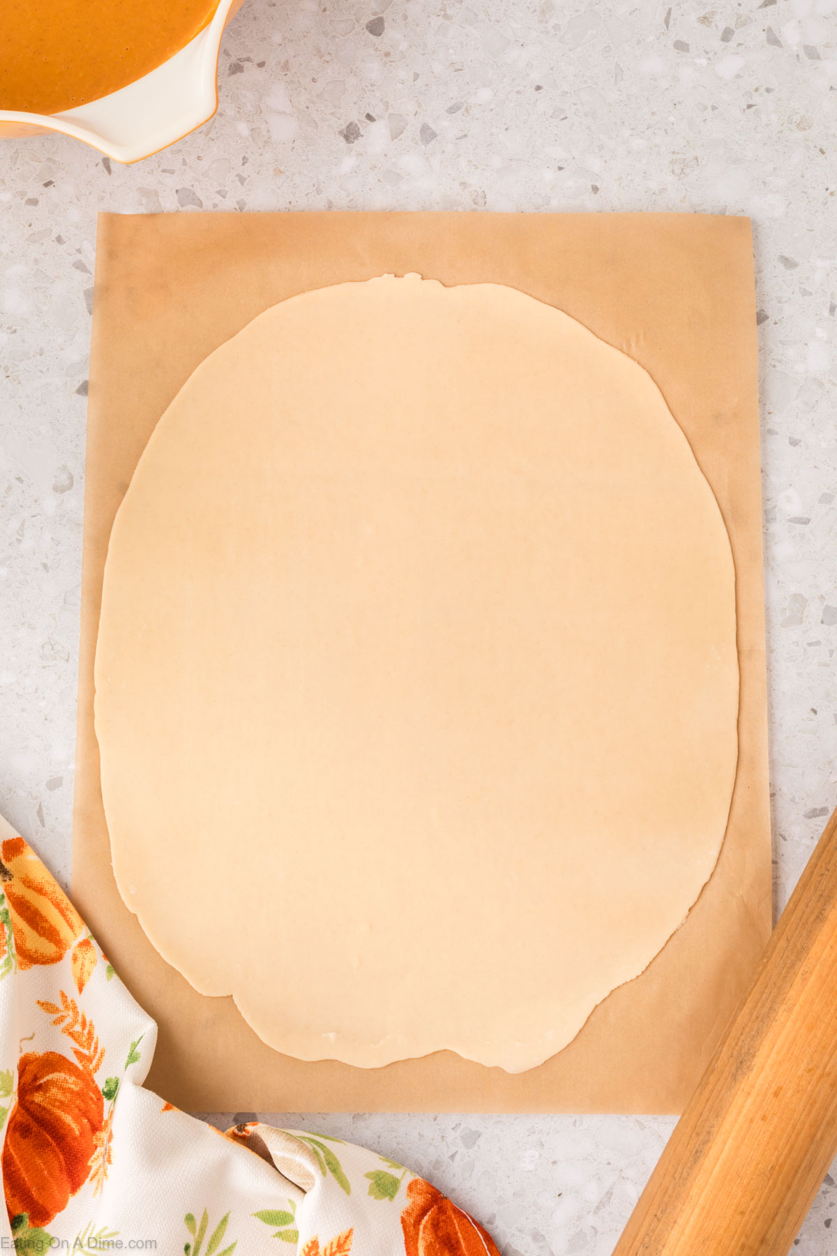 Rolling the pie crust dough on parchment paper with a rolling pin