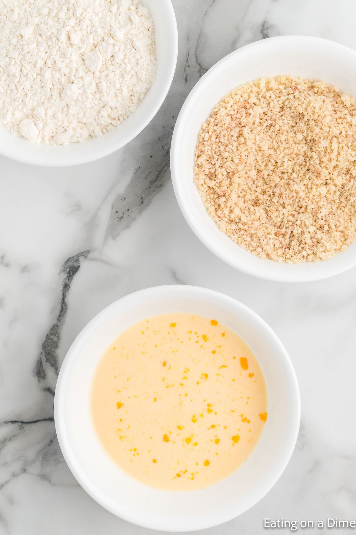 Placing the egg mixture, bread crumbs, and flour in three different bowls