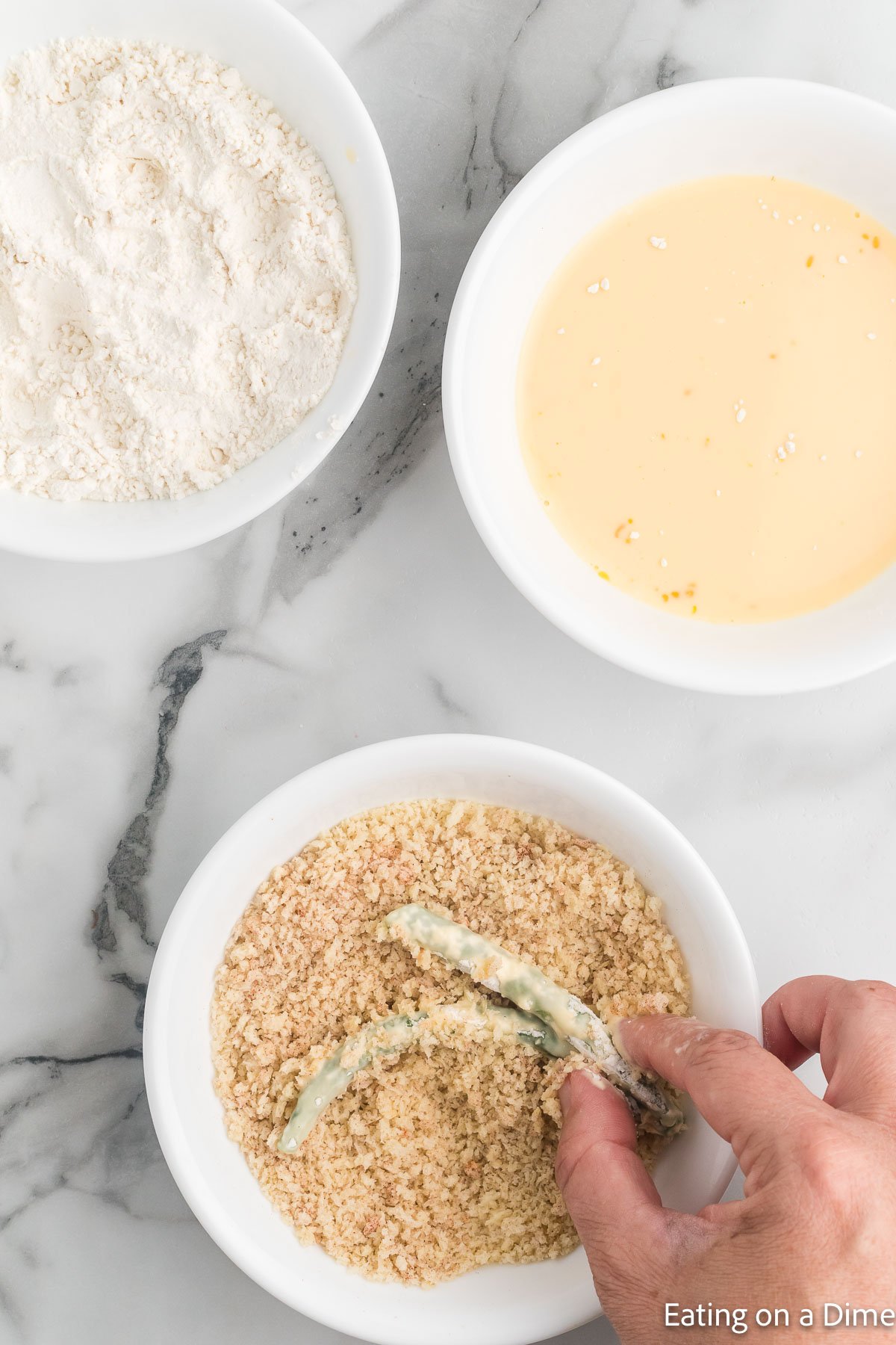 Coating the green beans with bread crumbs, egg mixture and flour