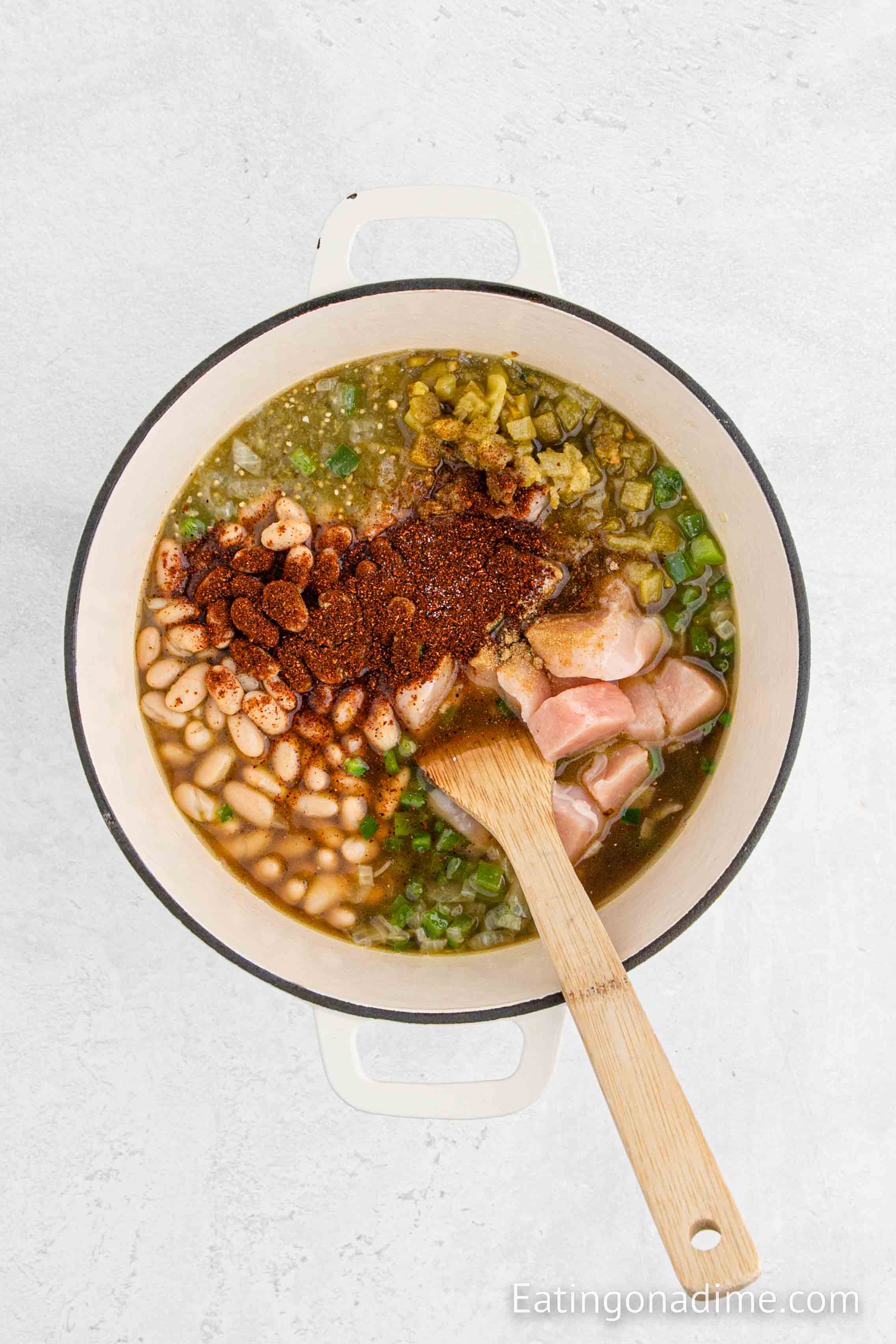 Adding the ingredients to a large pot and stirring with a wooden spoon