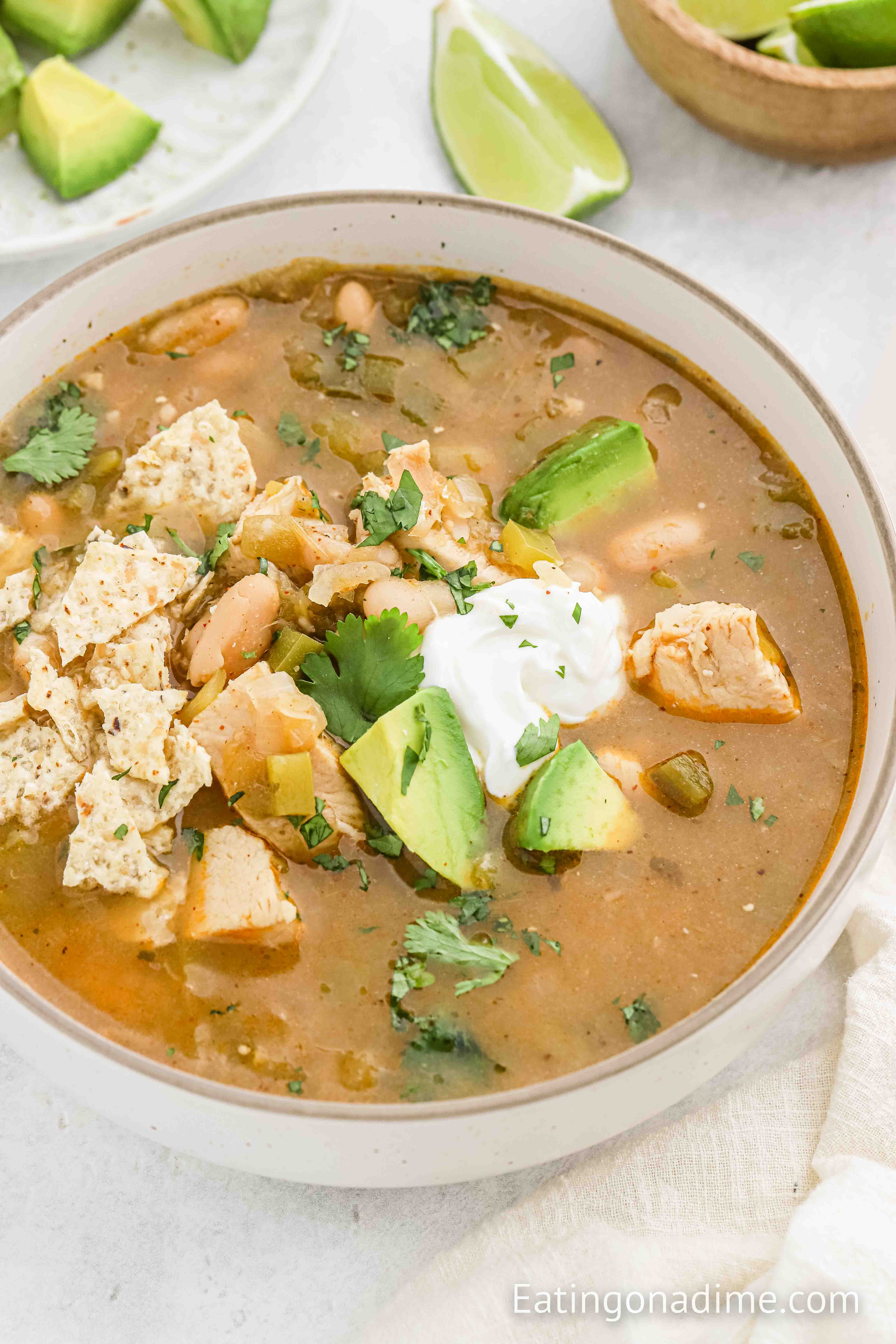 Green Chile Chicken Soup in a large bowl topped with slice avocados and sour cream