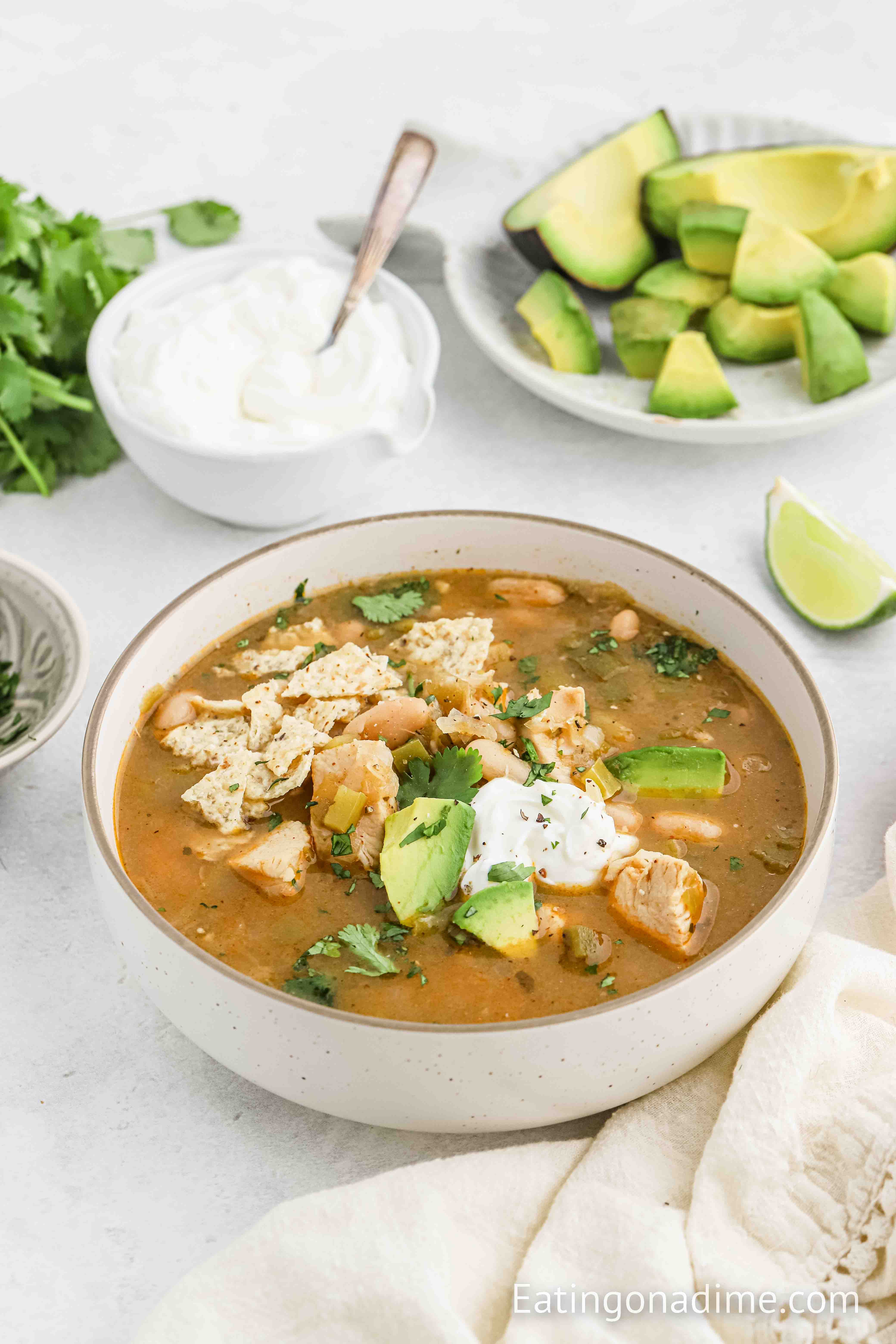 Green Chile Chicken Soup in a bowl topped with sour cream and slice avocados