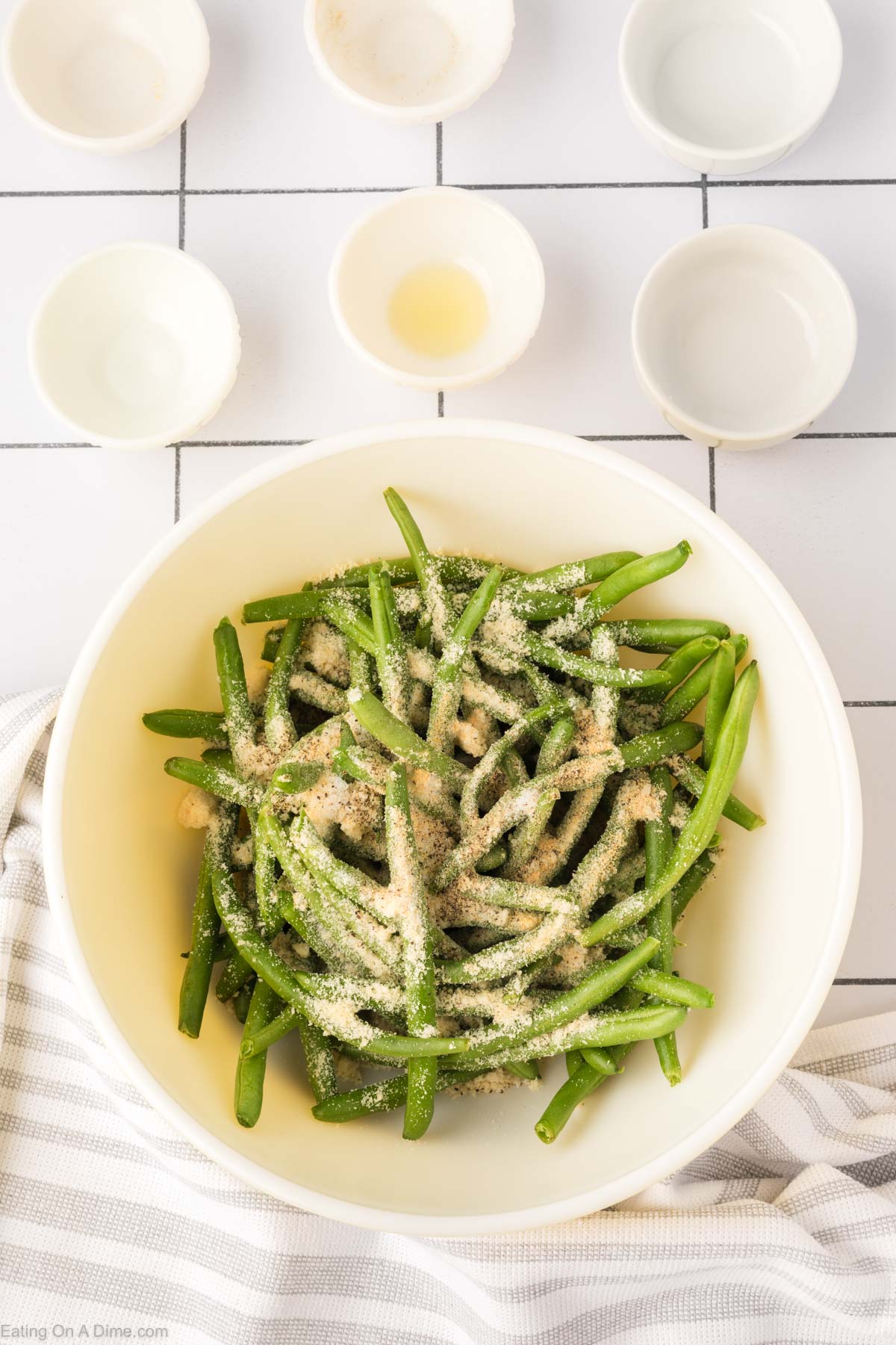 Placing the seasoning and oil on the green beans in a bowl