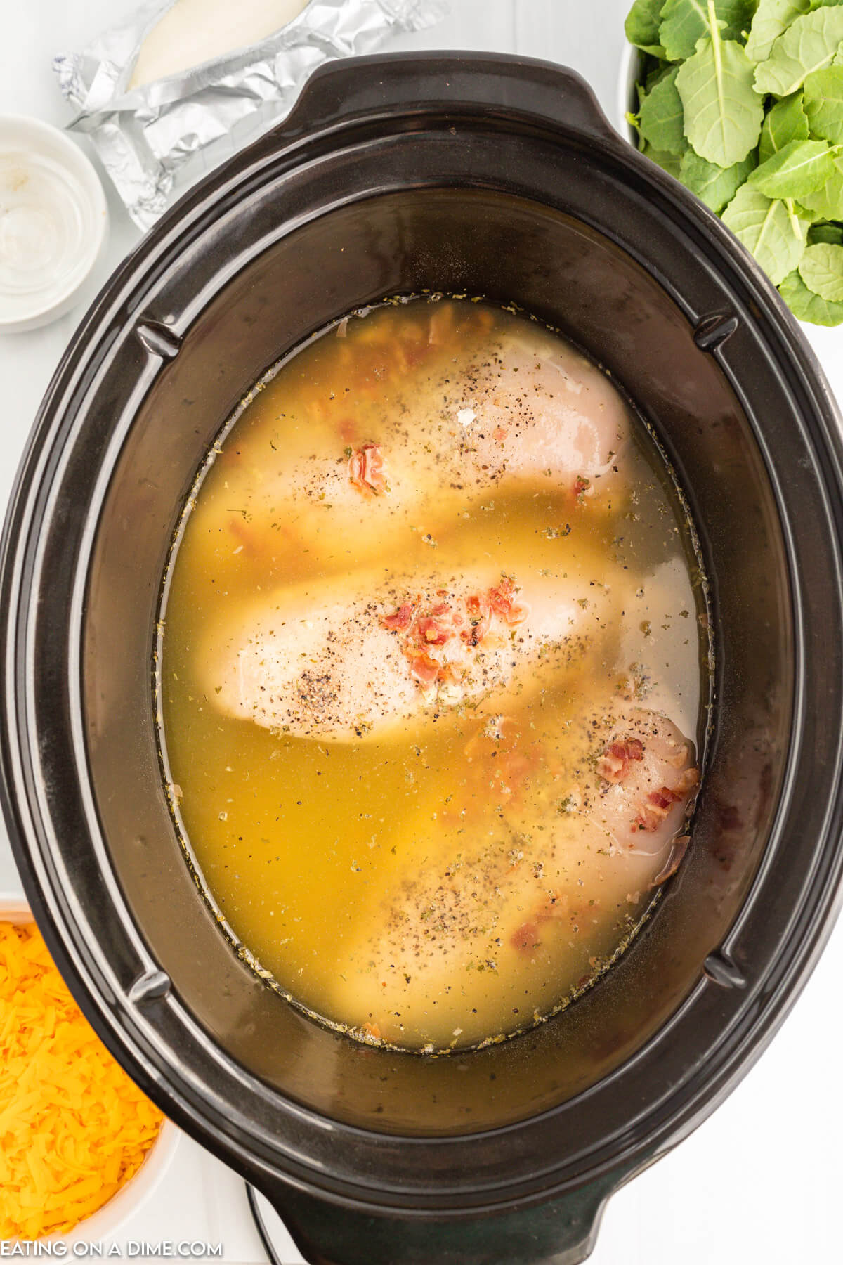 Placing chicken, broth, bacon, and seasoning in the slow cooker
