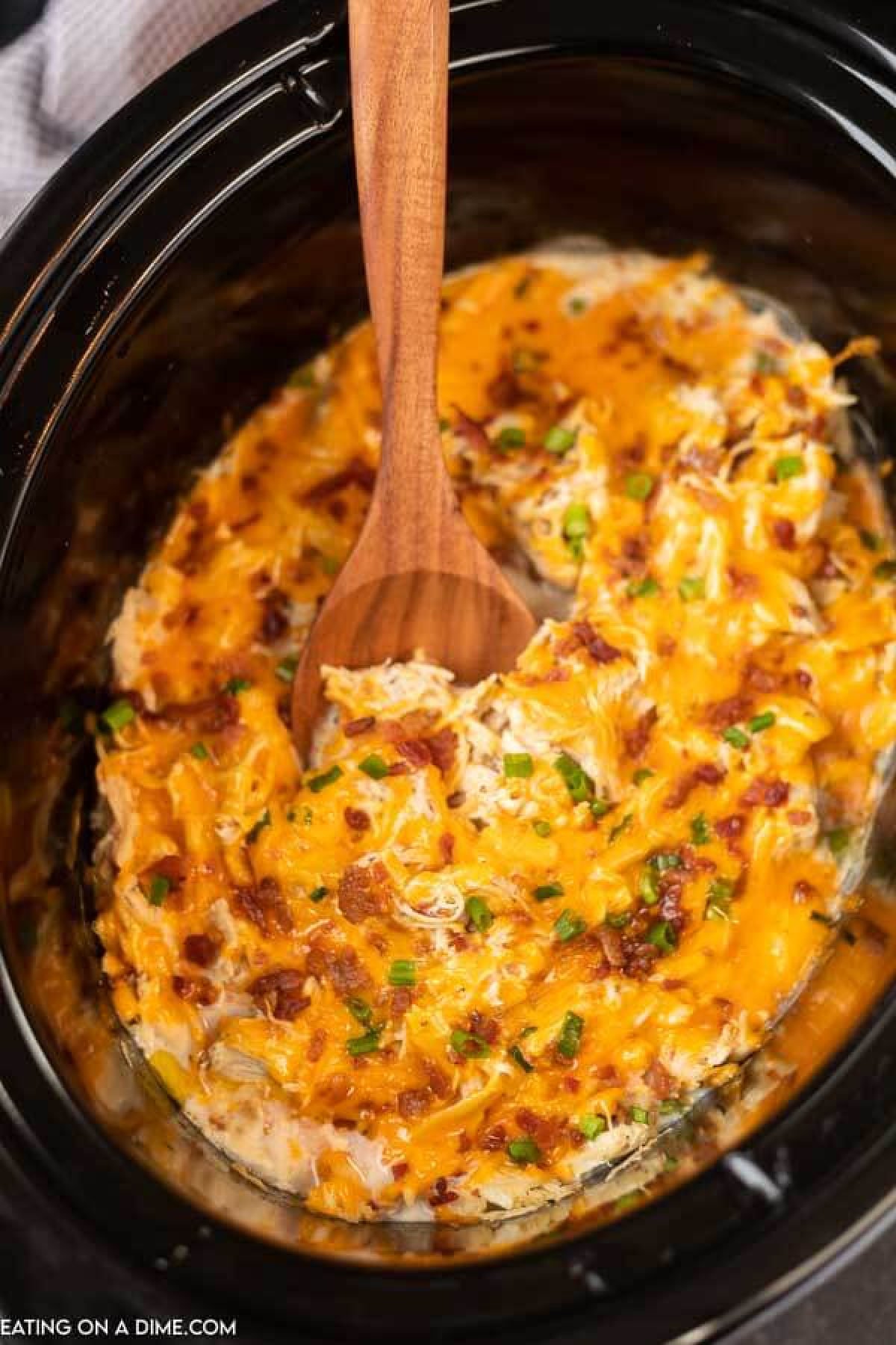 picture of crack chicken in slow cooker with a wooden spoon.