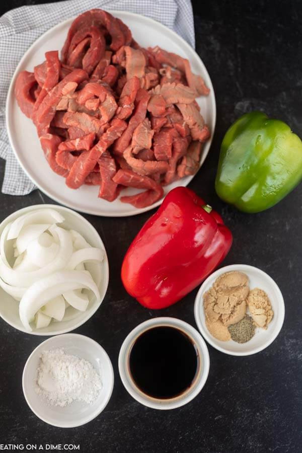 Ingredients to make crock pot pepper steak: sliced steak, red bell pepper, green bell pepper, sliced onions, soy sauce, cornstarch, ground ginger, garlic powder, pepper and brown sugar.  