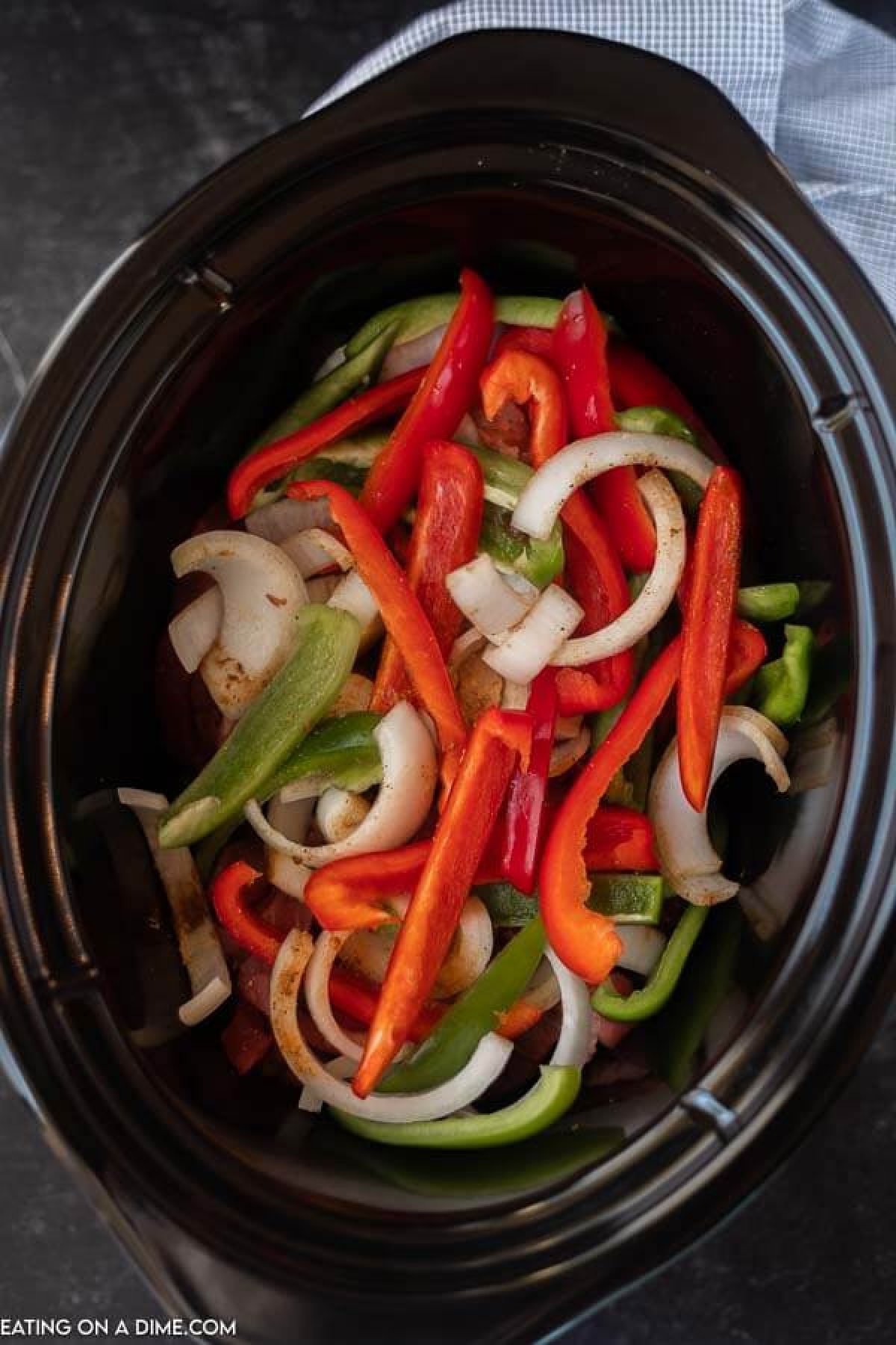 The beef, sliced onions, sliced bell peppers and seasonings in the crock pot.  