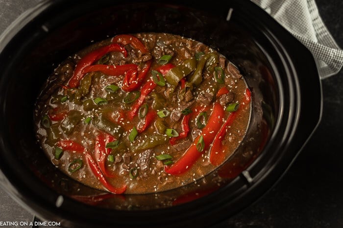 The pepper steak recipe in a black crock pot topped with sesame seeds. 