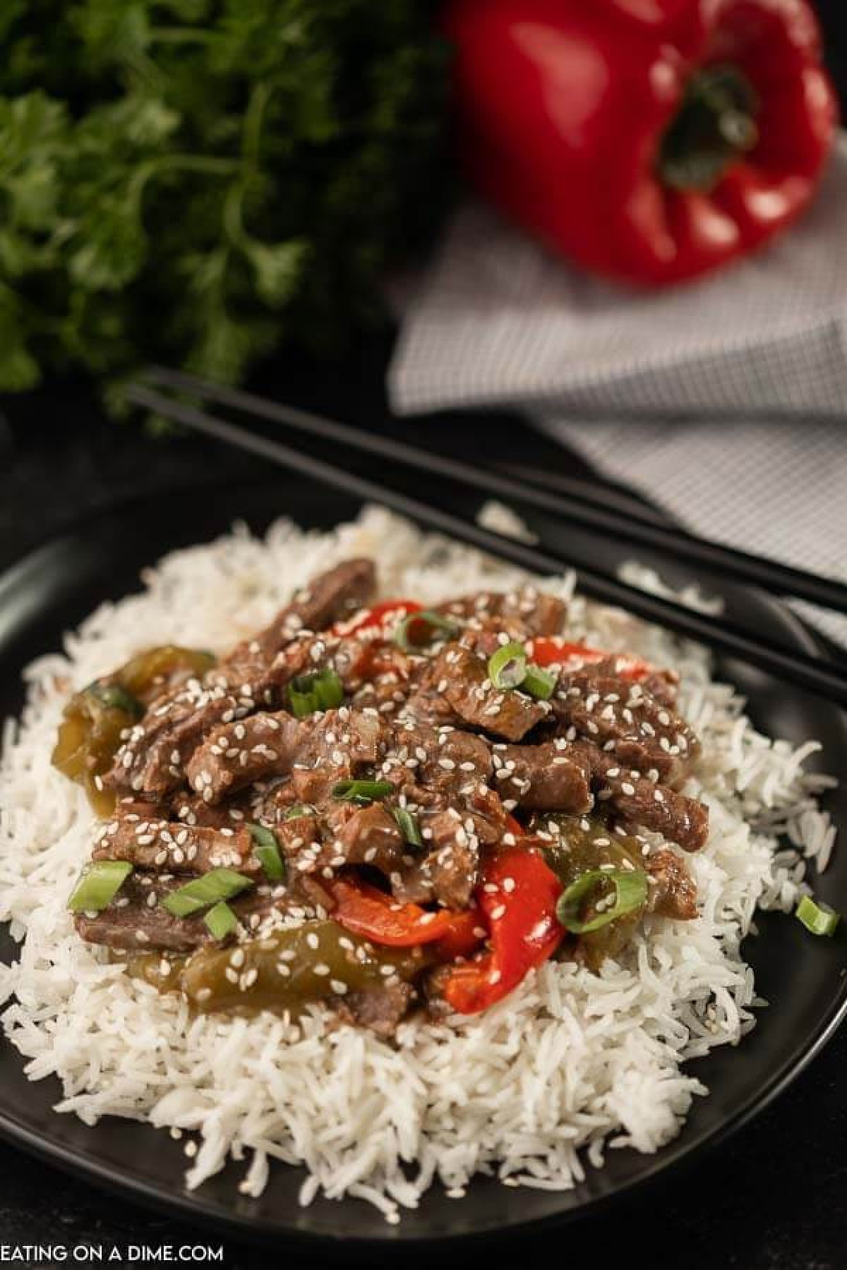 A black plate topped with rice and this crock pot pepper steak with peppers on top of the rice. 