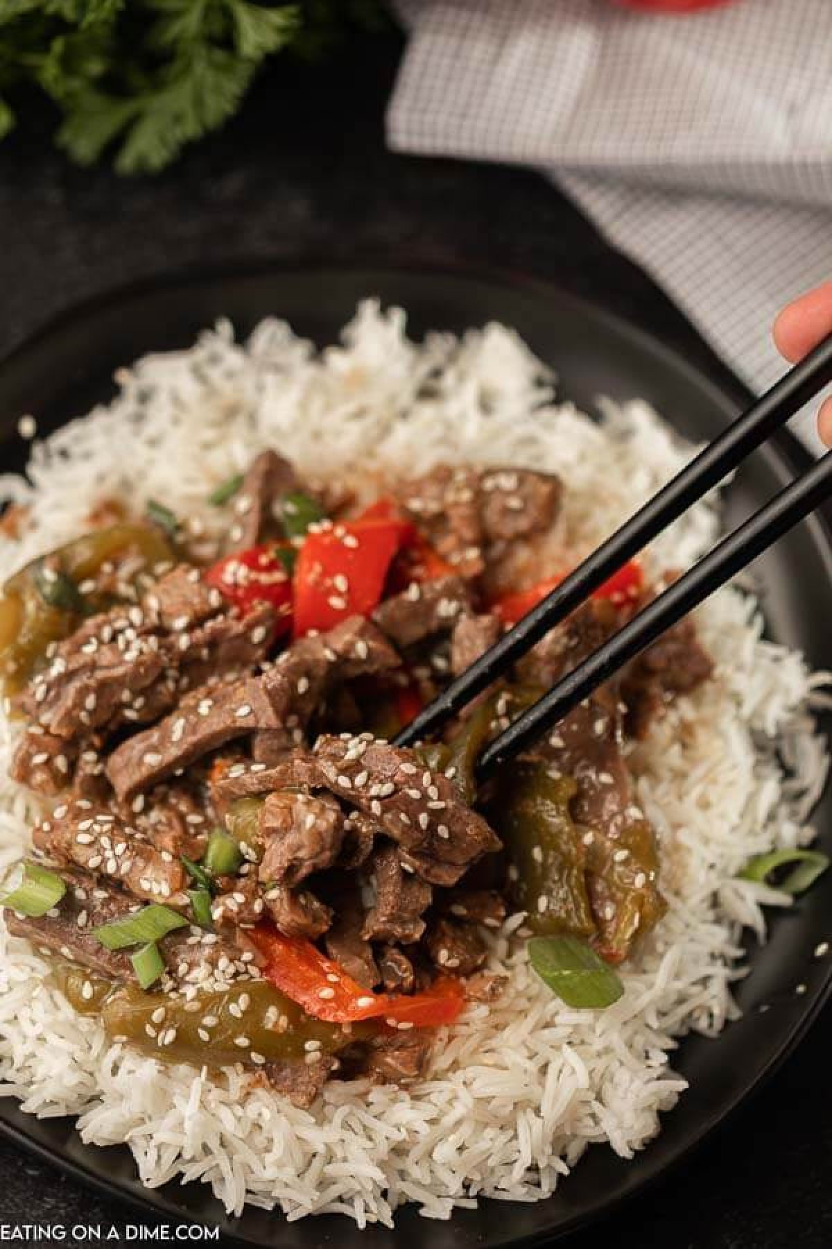 A plate filled with rice and then this crock pot pepper steak on top with chop sticks picking up some of the pepper steak. 