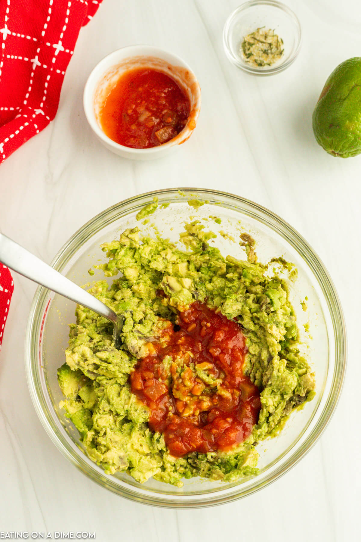 Mixing in salsa into the mashed avocados in a bowl