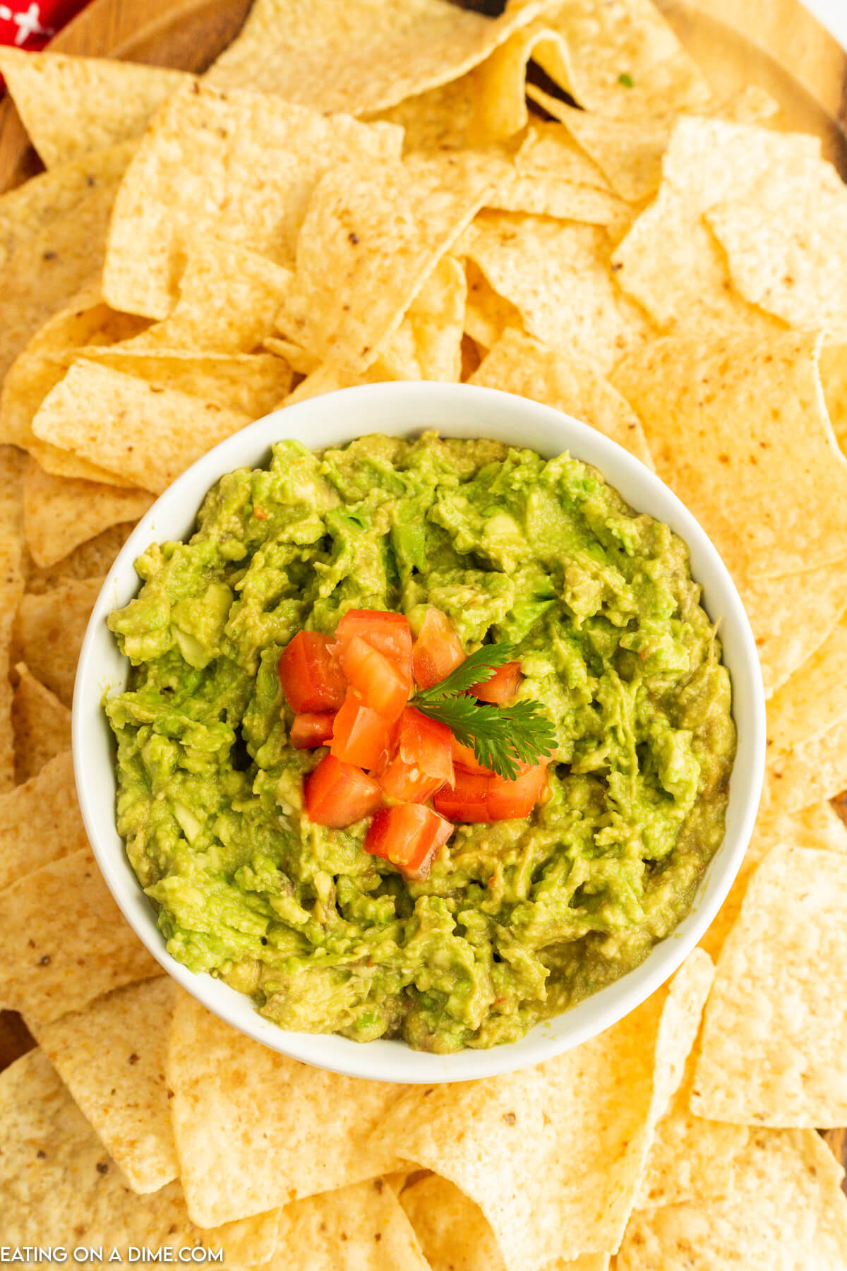 Guacamole in a white bowl topped with diced tomatoes and served with tortilla chips