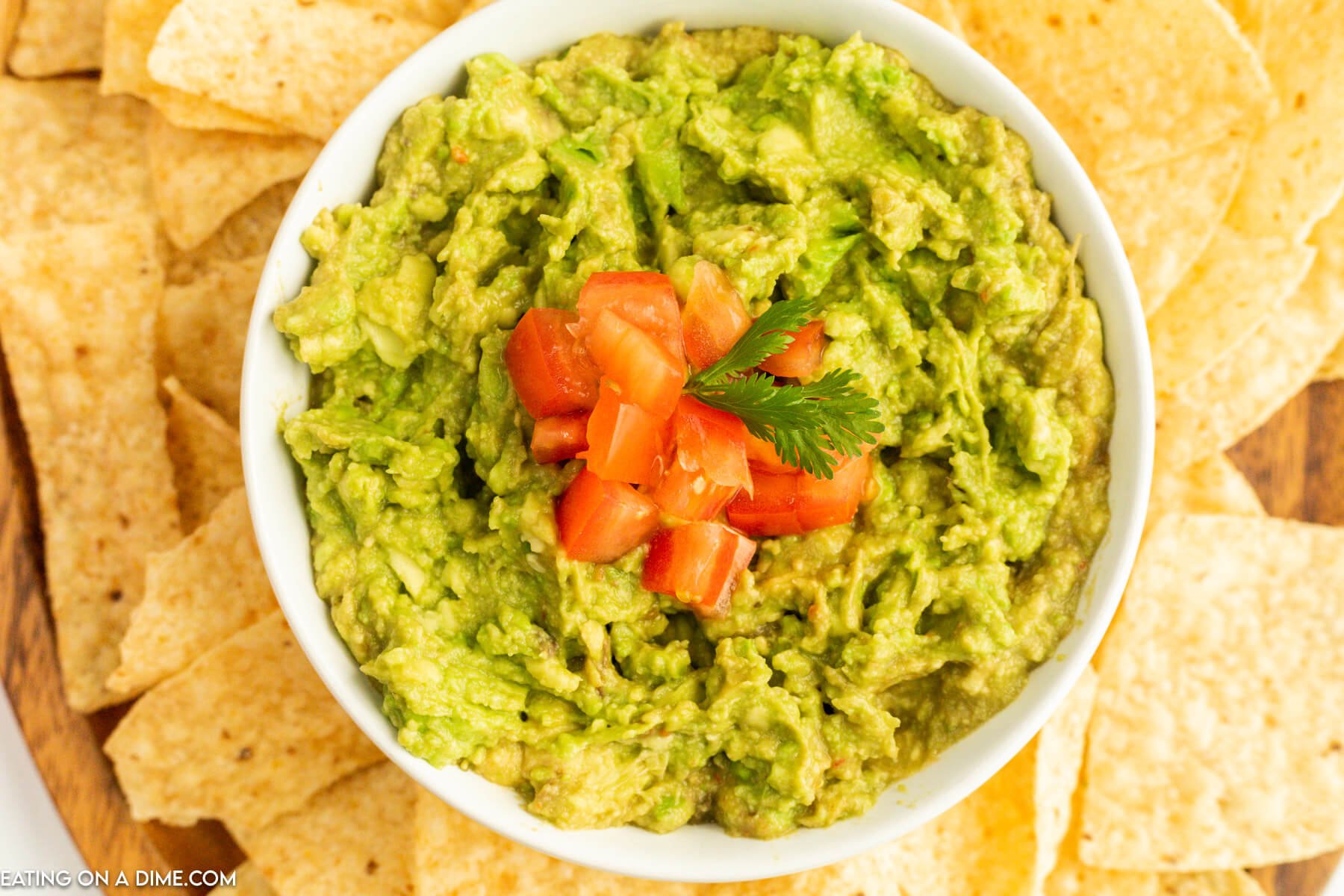 Guacamole Dip in a white bowl topped with diced tomatoes with tortilla chips on the side