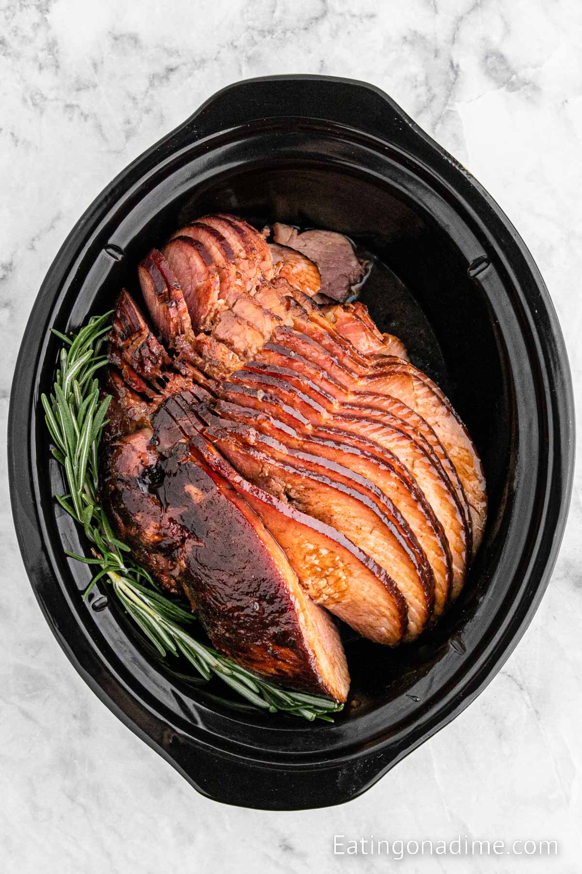 Cooked Spiral Ham in the crockpot with a rosemary sprig on the side
