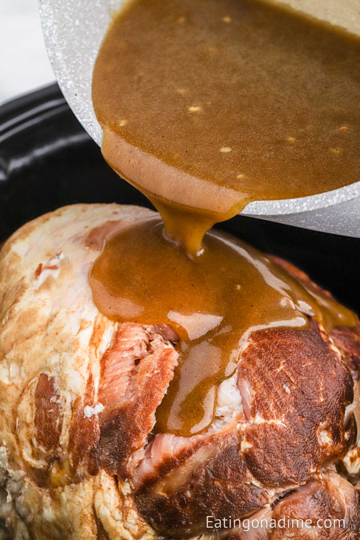 Pouring the glaze over the top of the ham in the slow cooker
