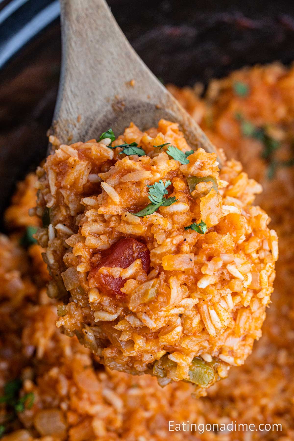 Spanish rice in a slow cooker with a serving on a wooden spoon