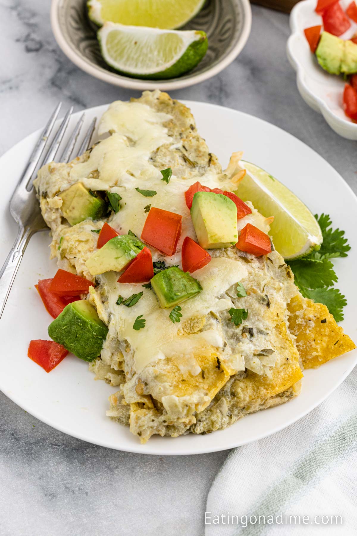 A serving of chicken enchiladas on a plate topped with diced avocado and diced tomatoes