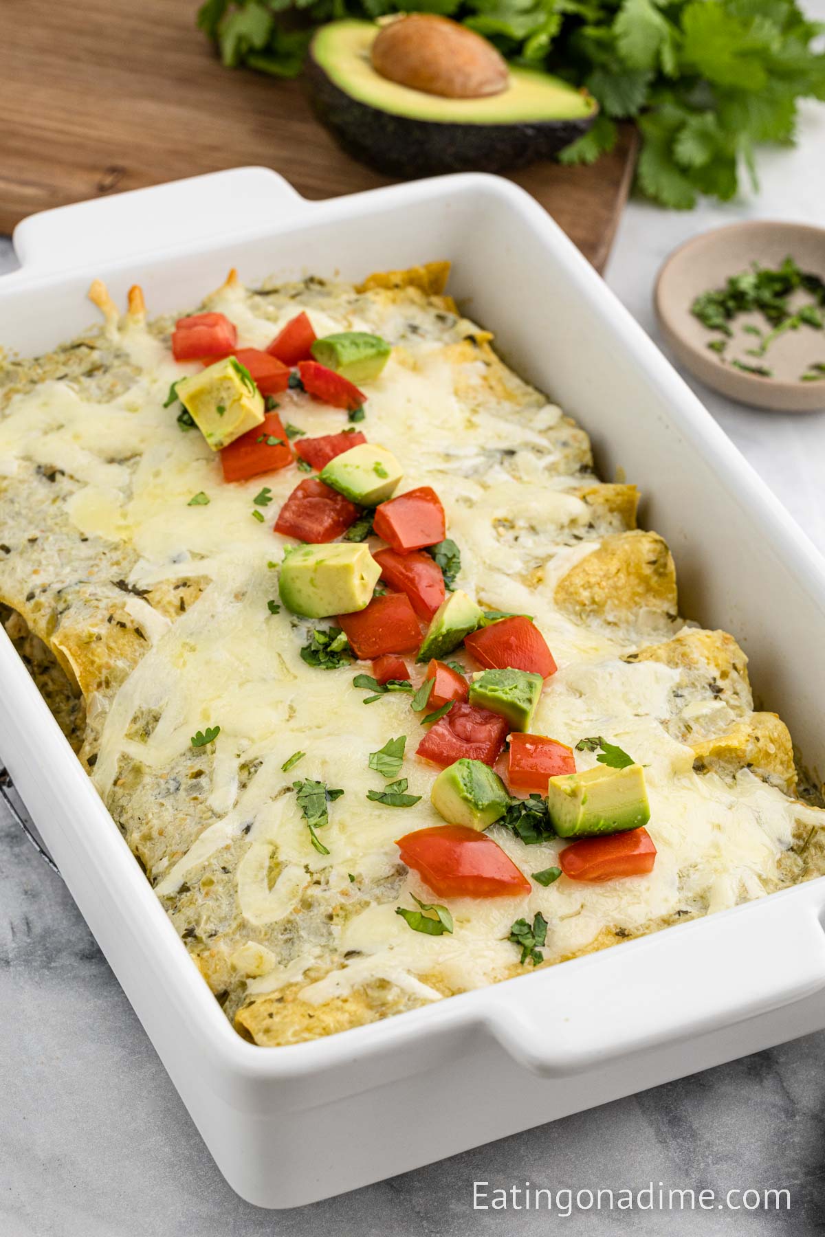 Chicken enchiladas in a baking dish topped with diced avocado and diced tomatoes