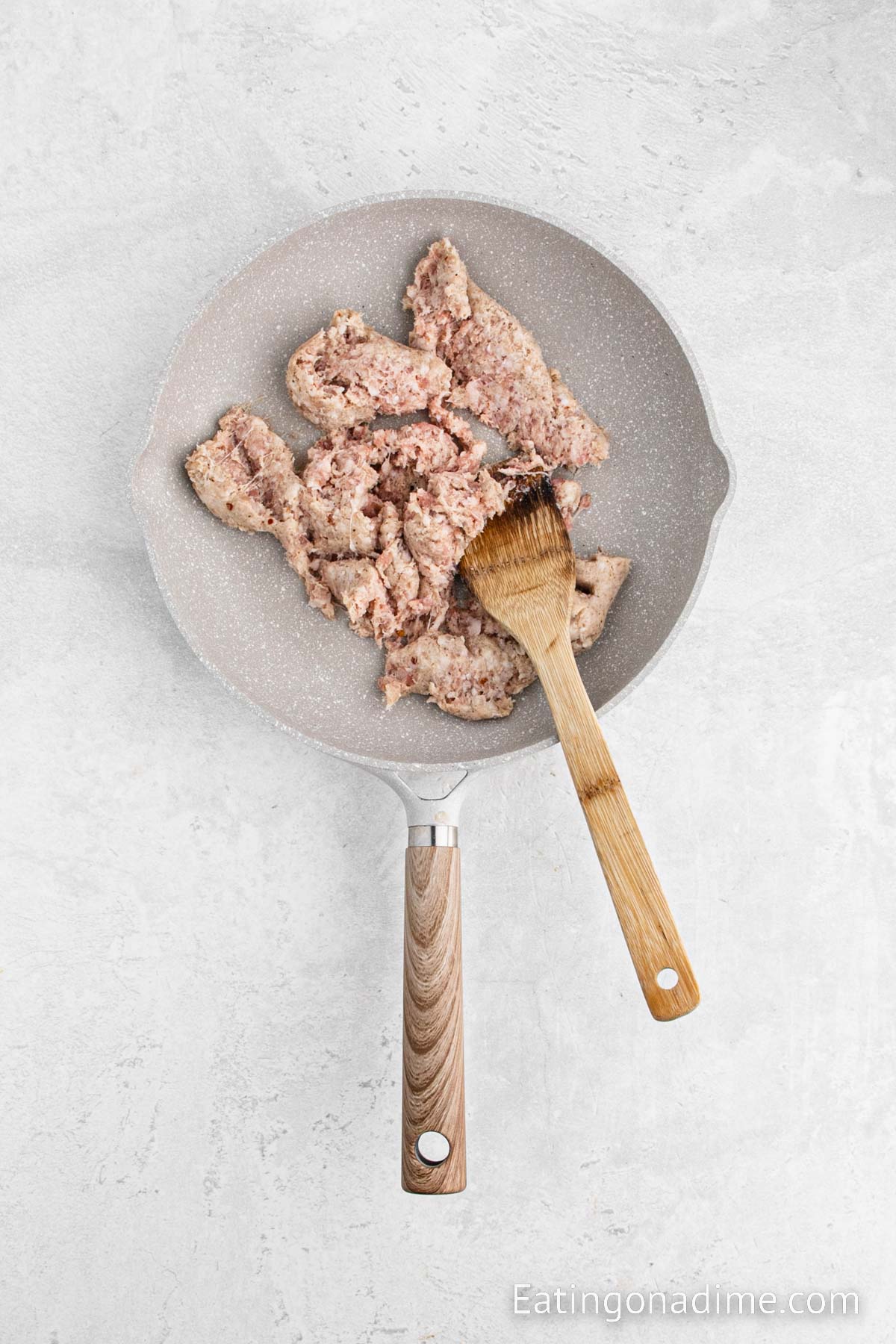 Cooking sausage in a skillet with a wooden spoon