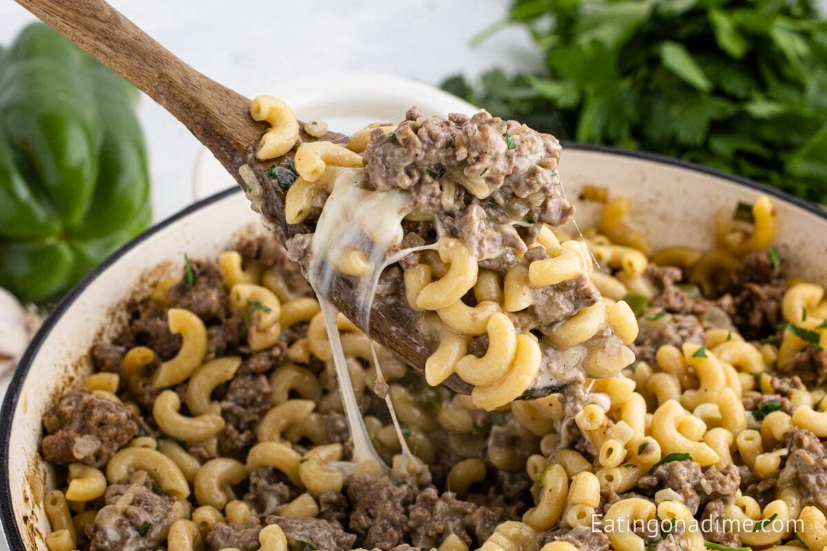 Philly cheesesteak pasta in a large skillet with a serving on a wooden spoon.