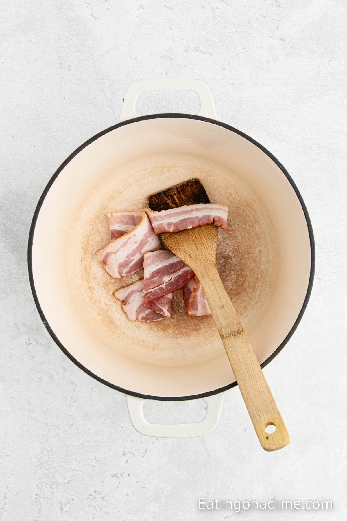 Cooking bacon in the large pot with a wooden spoon