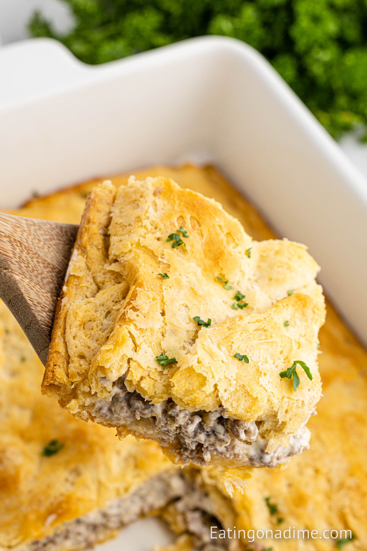 Close up image of a slice of sausage cream cheese casserole on a wooden spoon