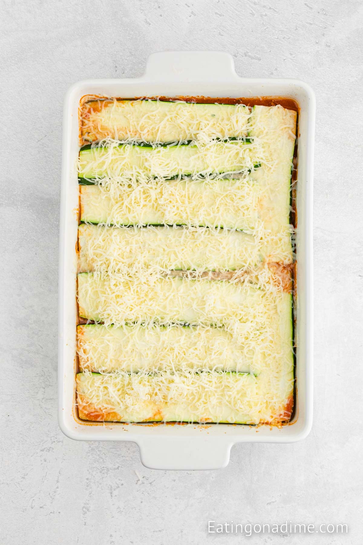 Topping the zucchini lasagna with shredded cheese