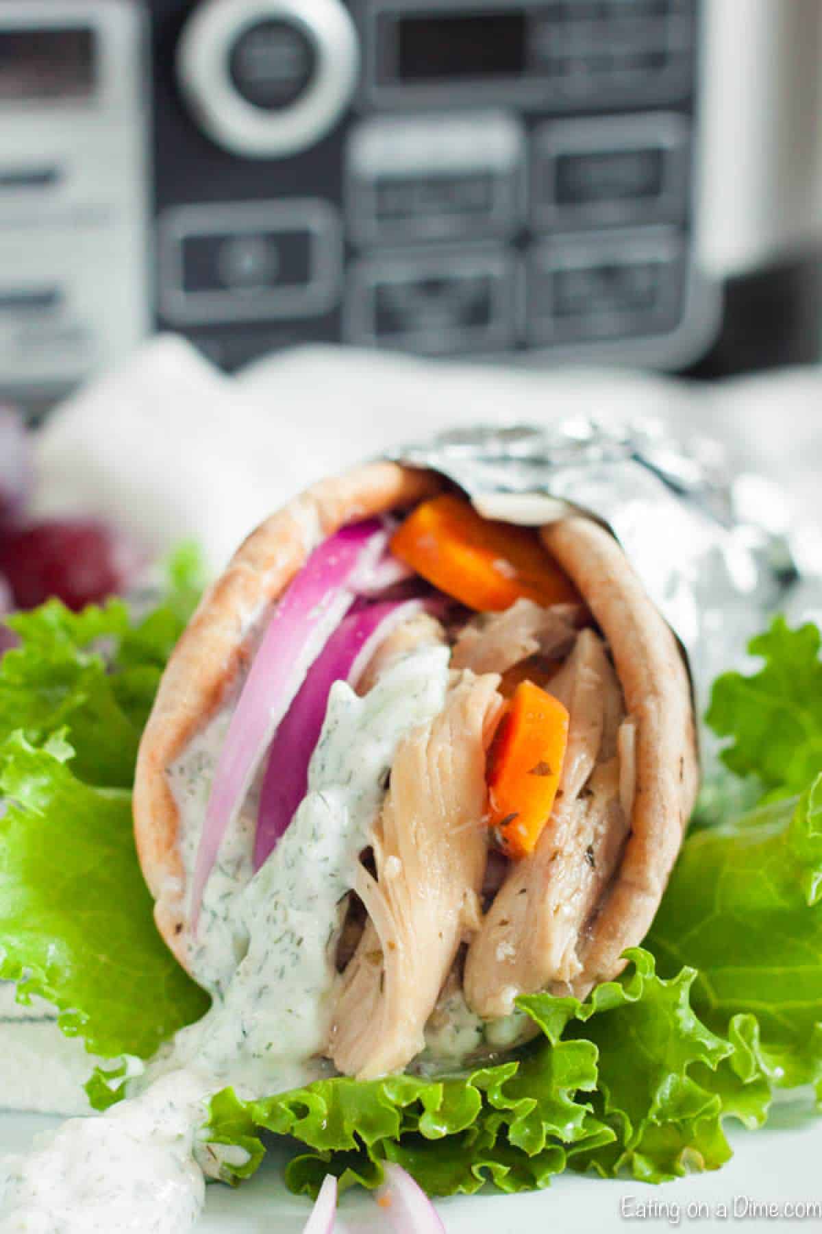 Chicken Gyro with Tzatziki Sauce in a pita bread wrapped in foil topped with onion and tomato