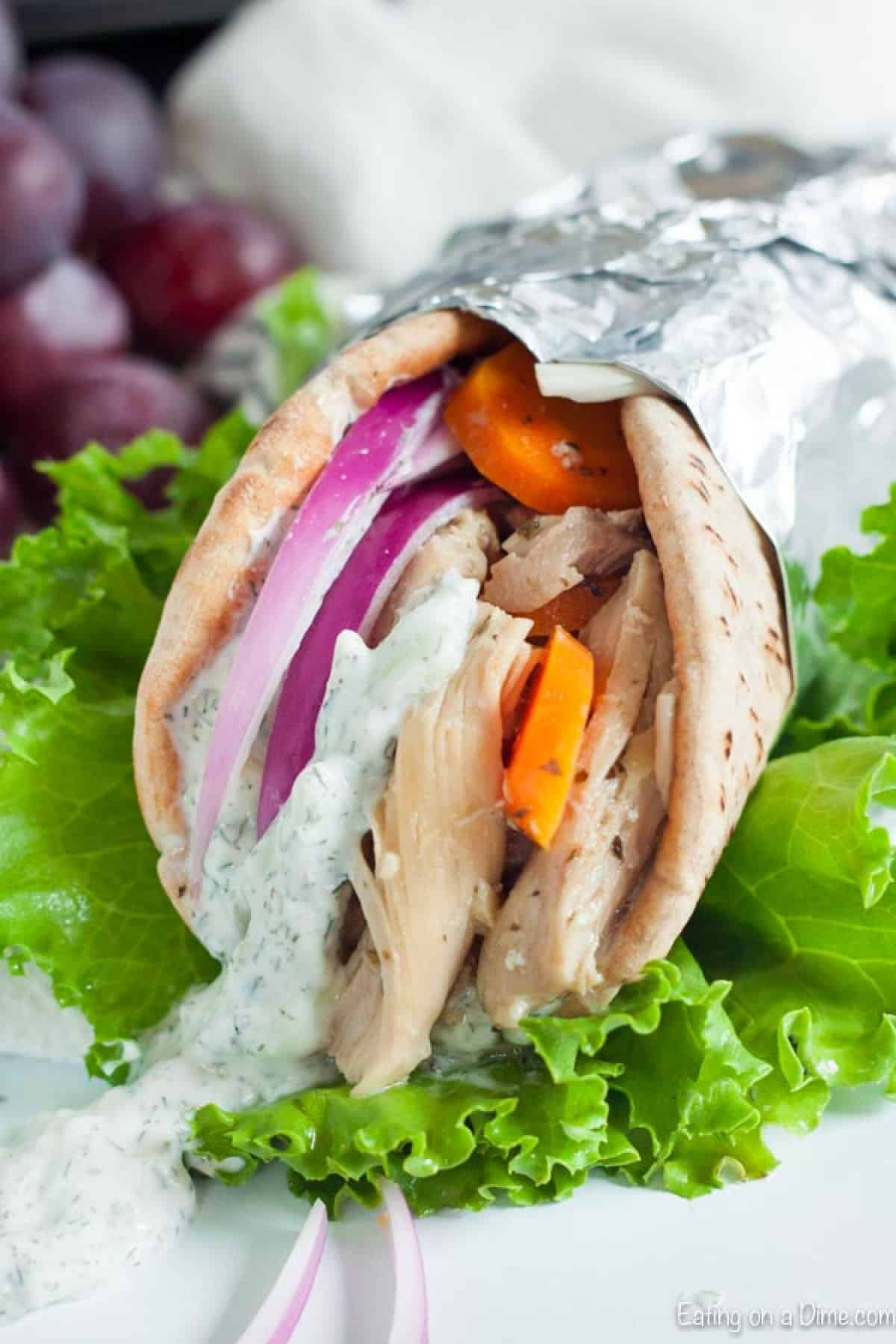 Chicken Gyro with Tzatziki Sauce in a pita bread wrapped in foil topped with onion and tomato