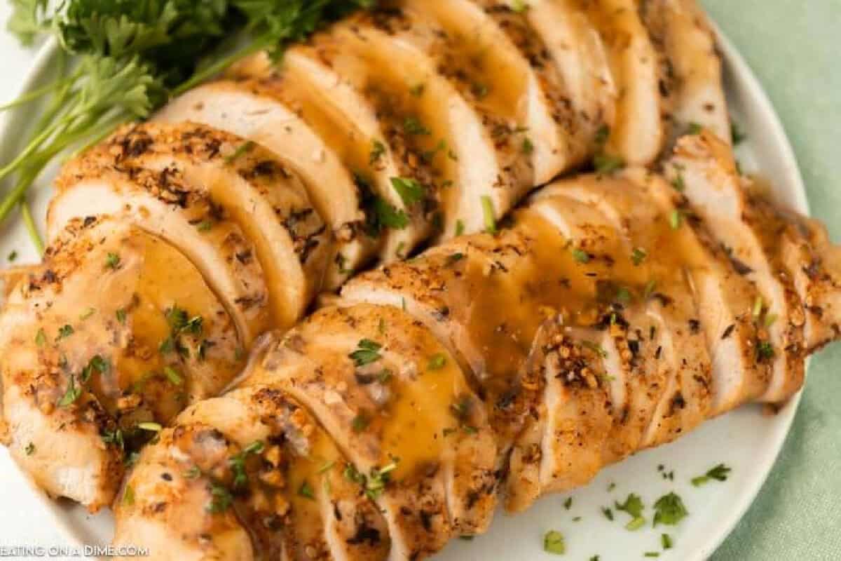 Sliced, seasoned chicken breasts topped with a golden herb sauce, garnished with chopped parsley, served on a white plate with fresh parsleyโan elegant dish that also works beautifully with slow cooker turkey breast.